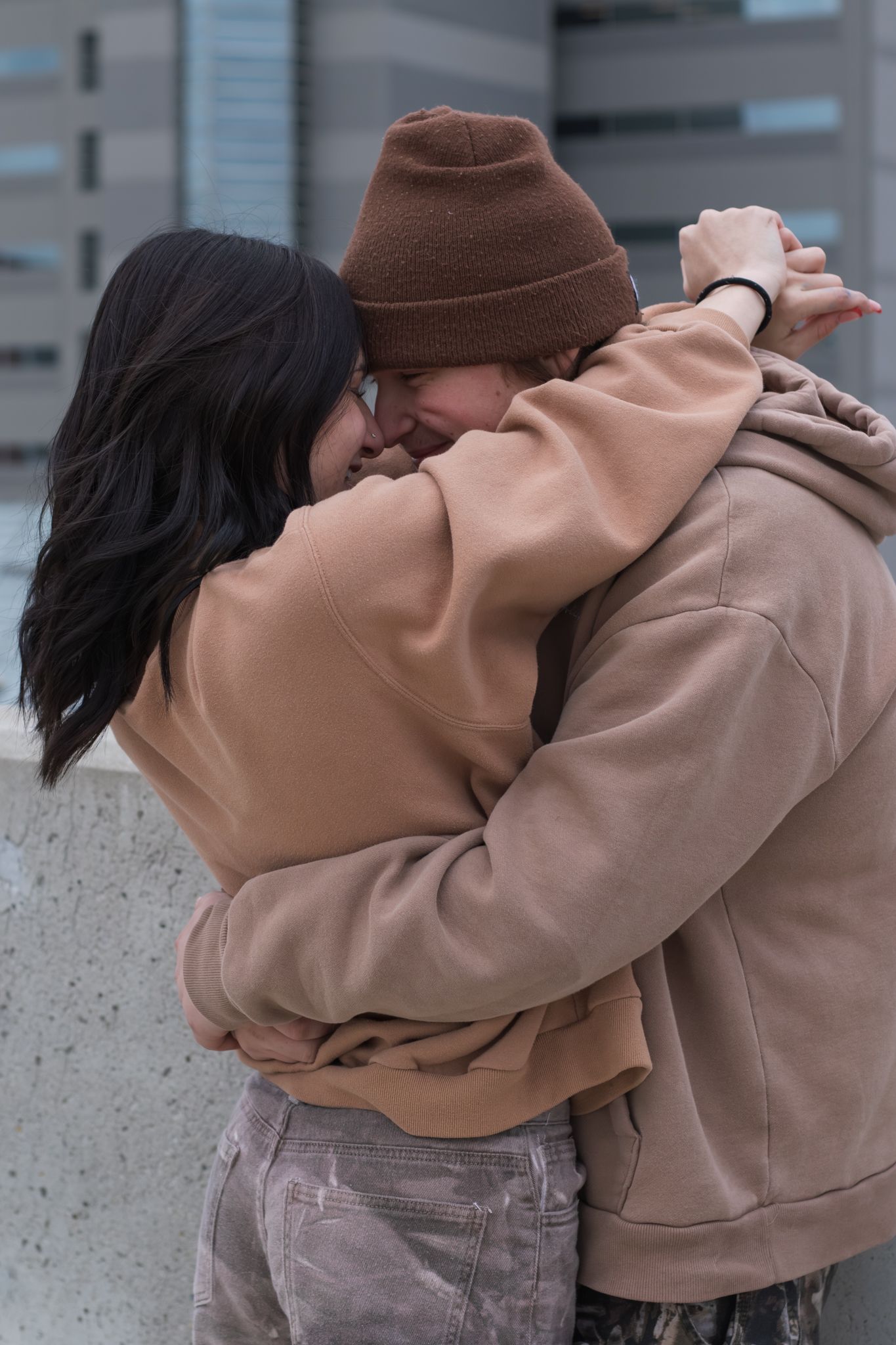Tender moment between couple in matching beige outfits against urban setting.