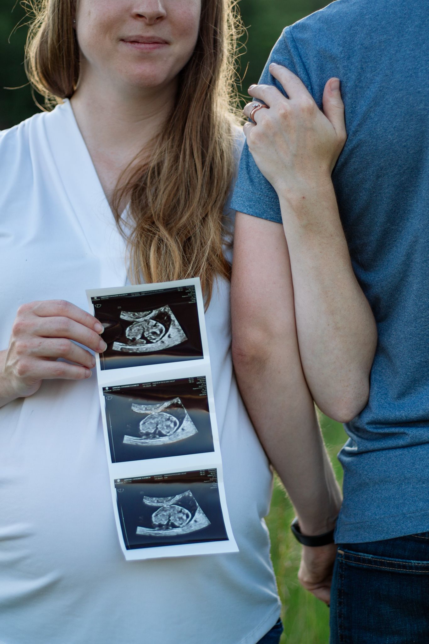 A couple smiling while showing ultrasound photos in natural lighting.