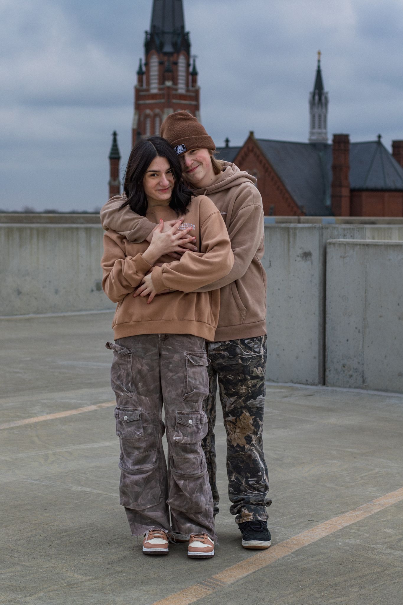 Couple in matching casual wear pose together with Gothic architecture in background.