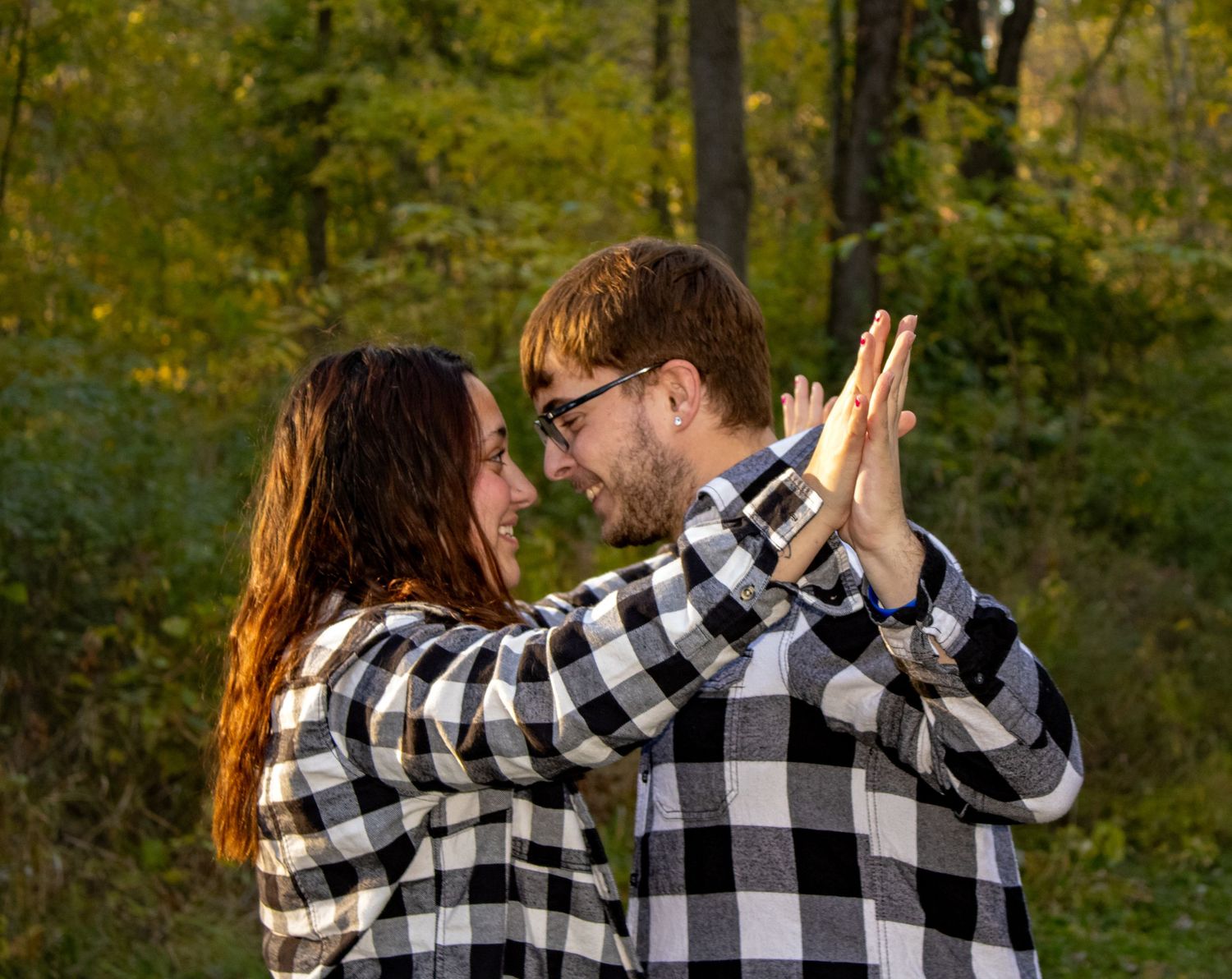 Couple in matching buffalo plaid shirts sharing affectionate moments in autumn woods.