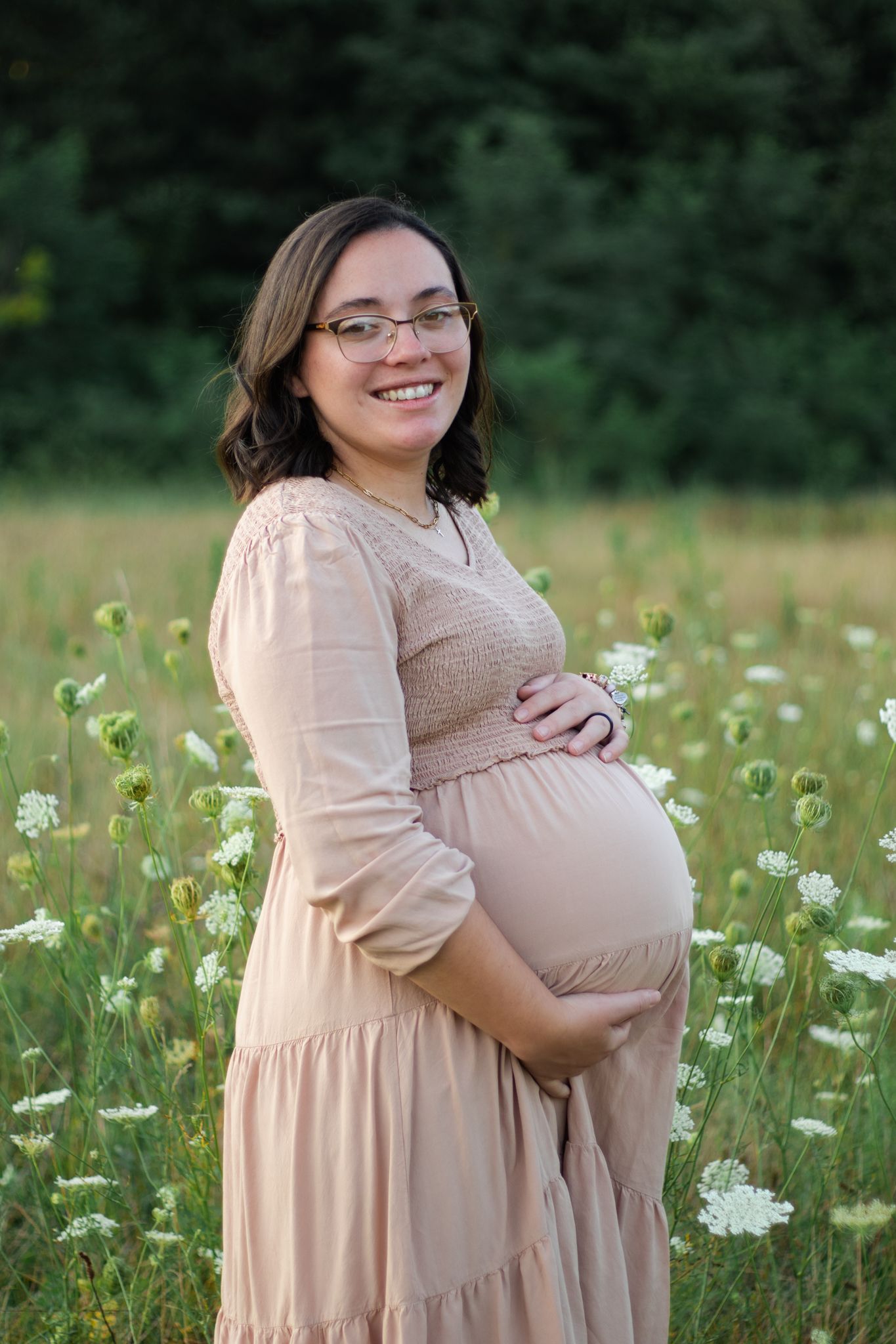 Beautiful maternity portraits in blooming wildflower field wearing beige dress.