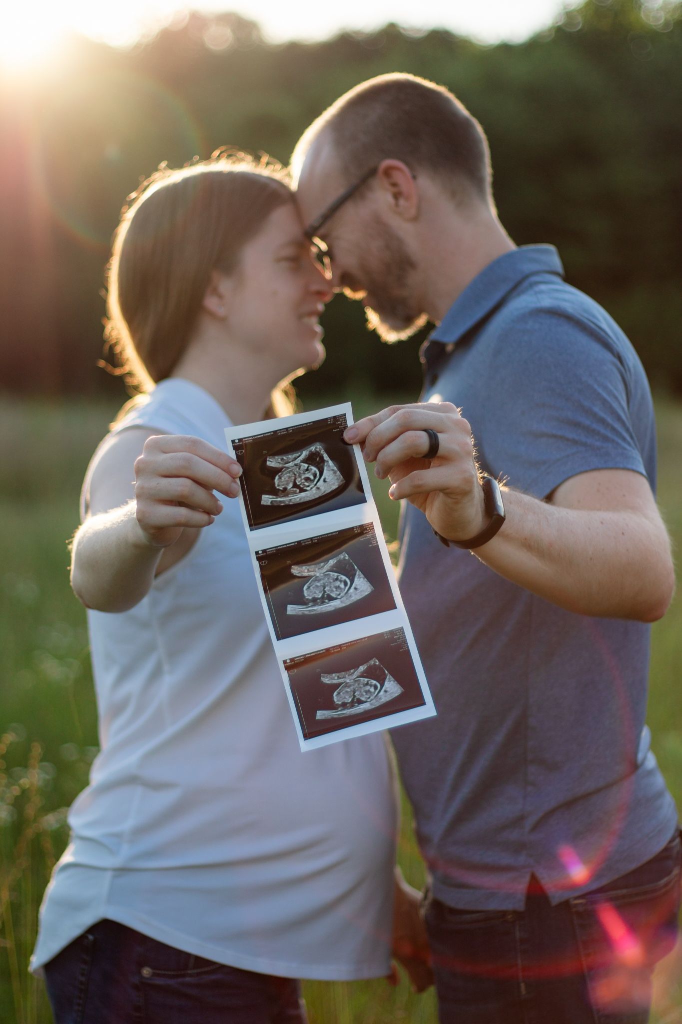 A couple sharing ultrasound photos in a sunlit field.