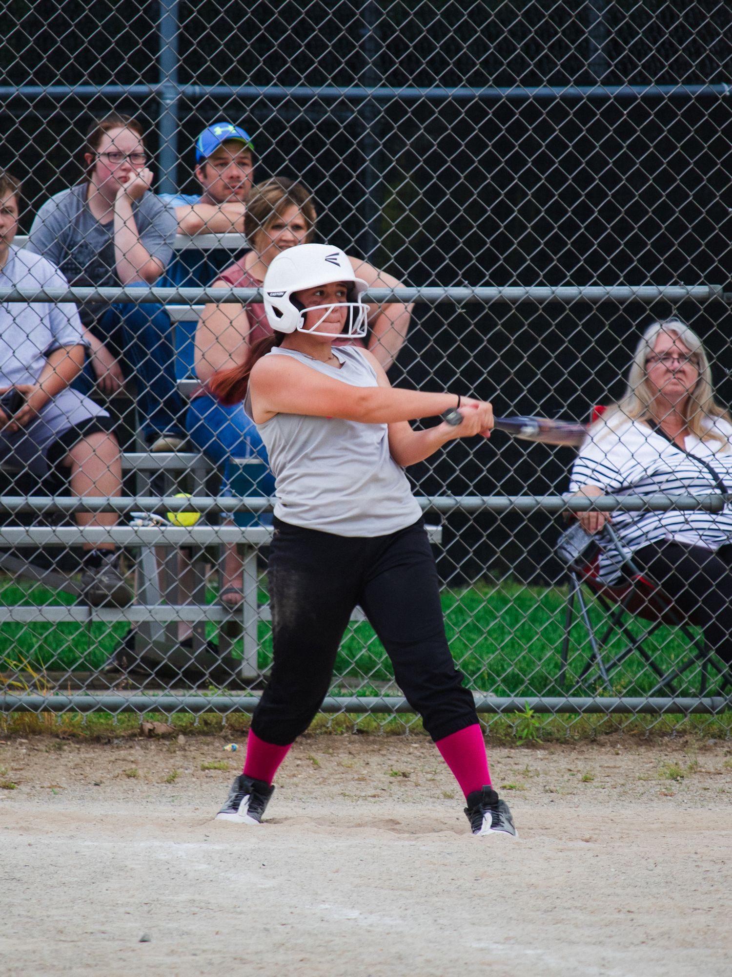 Softball batter in white helmet takes powerful swing during game on dirt field.