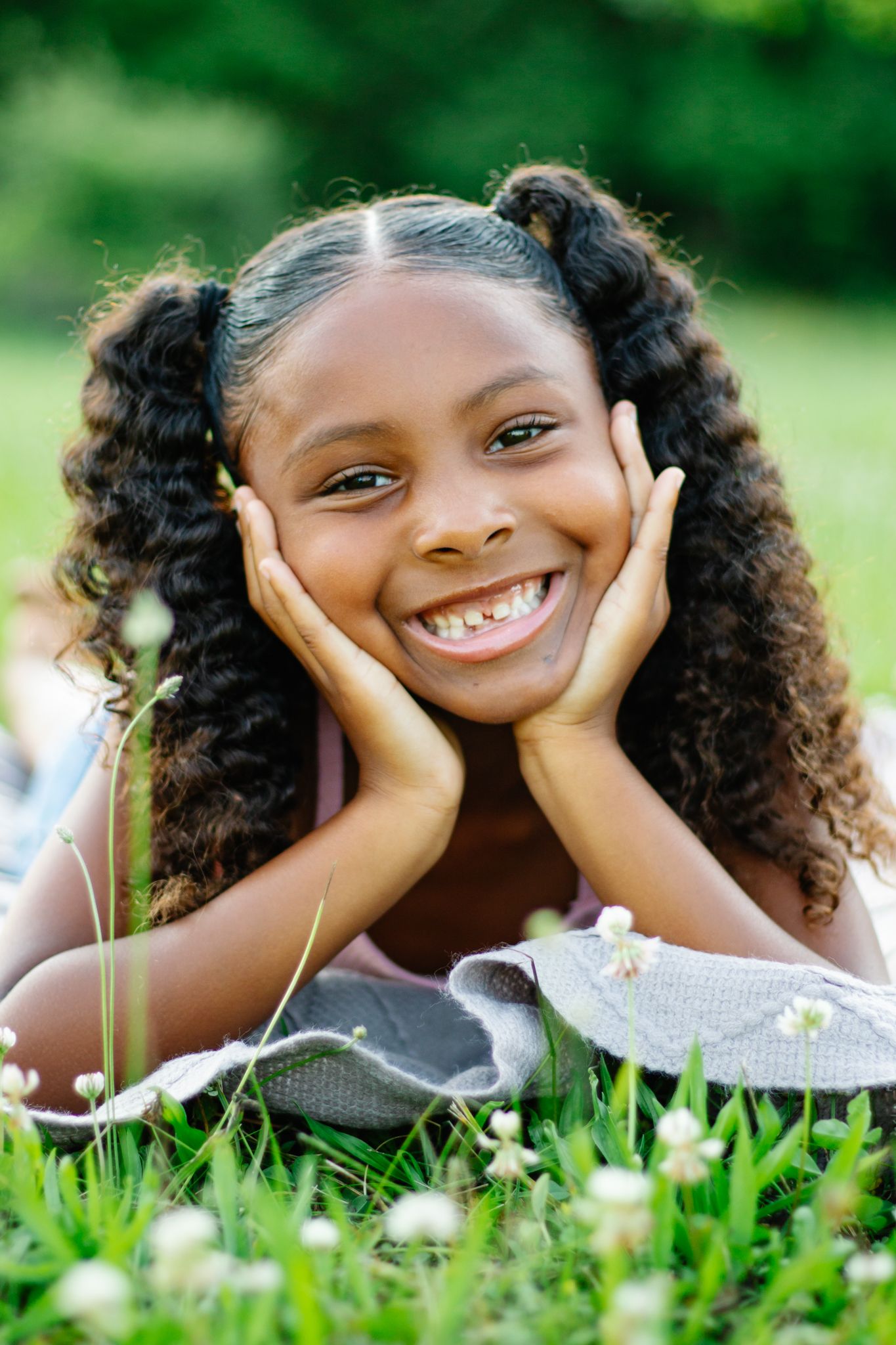 Child resting head in hands while laying on grass with joyful expression.