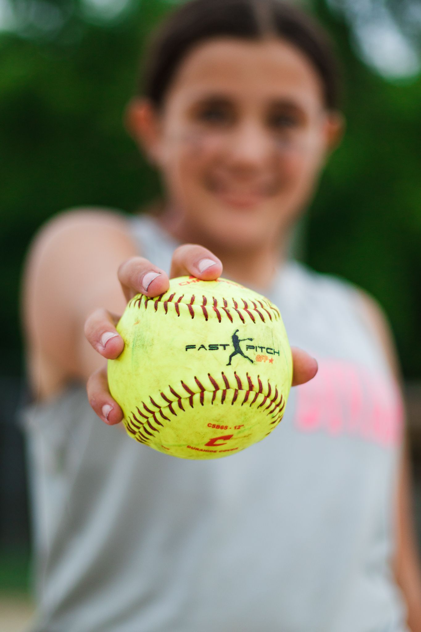 Close-up of bright yellow softball being held up against blurred background.