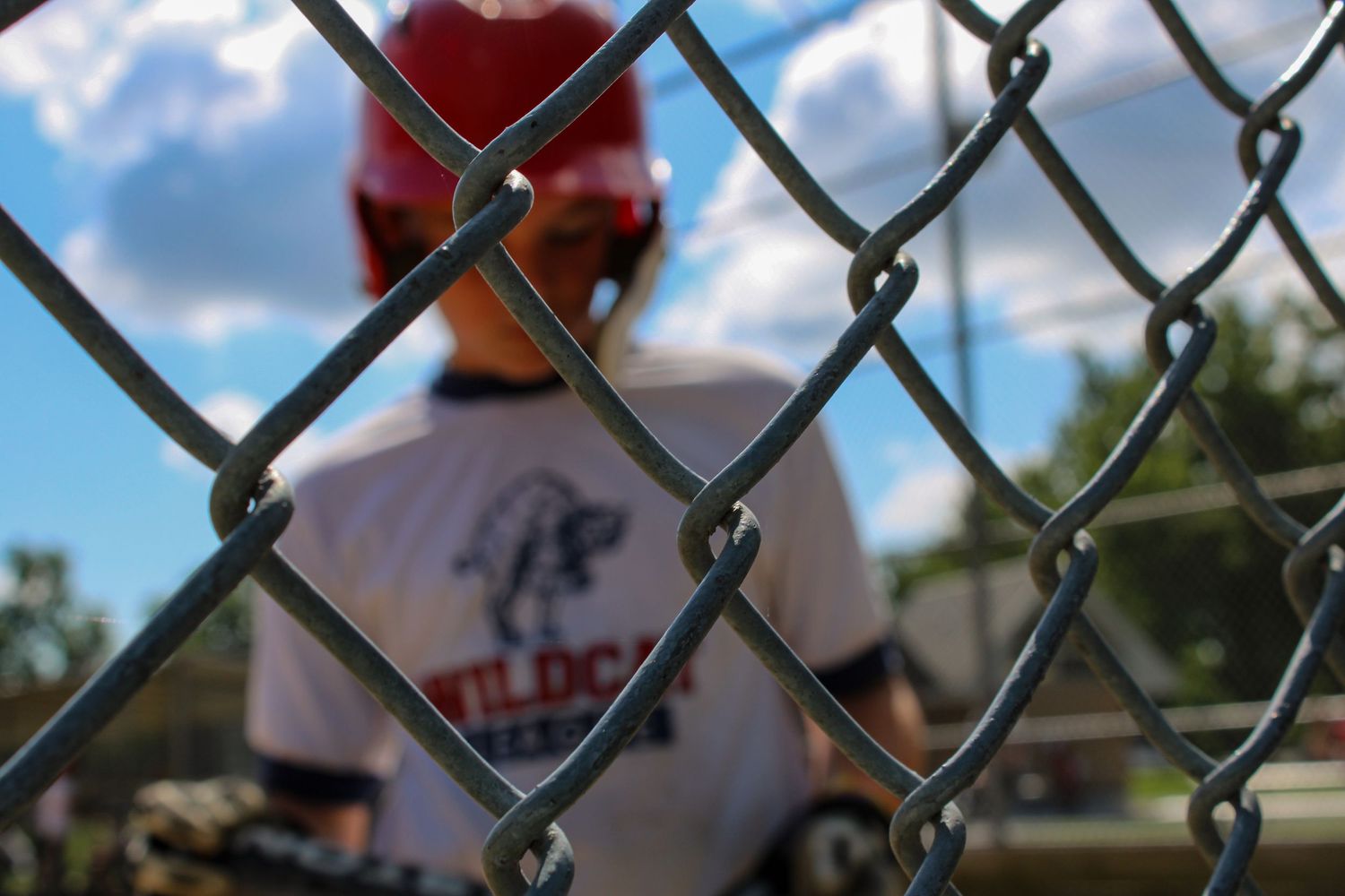 Close-up view through chain link fence of baseball field with players in background.