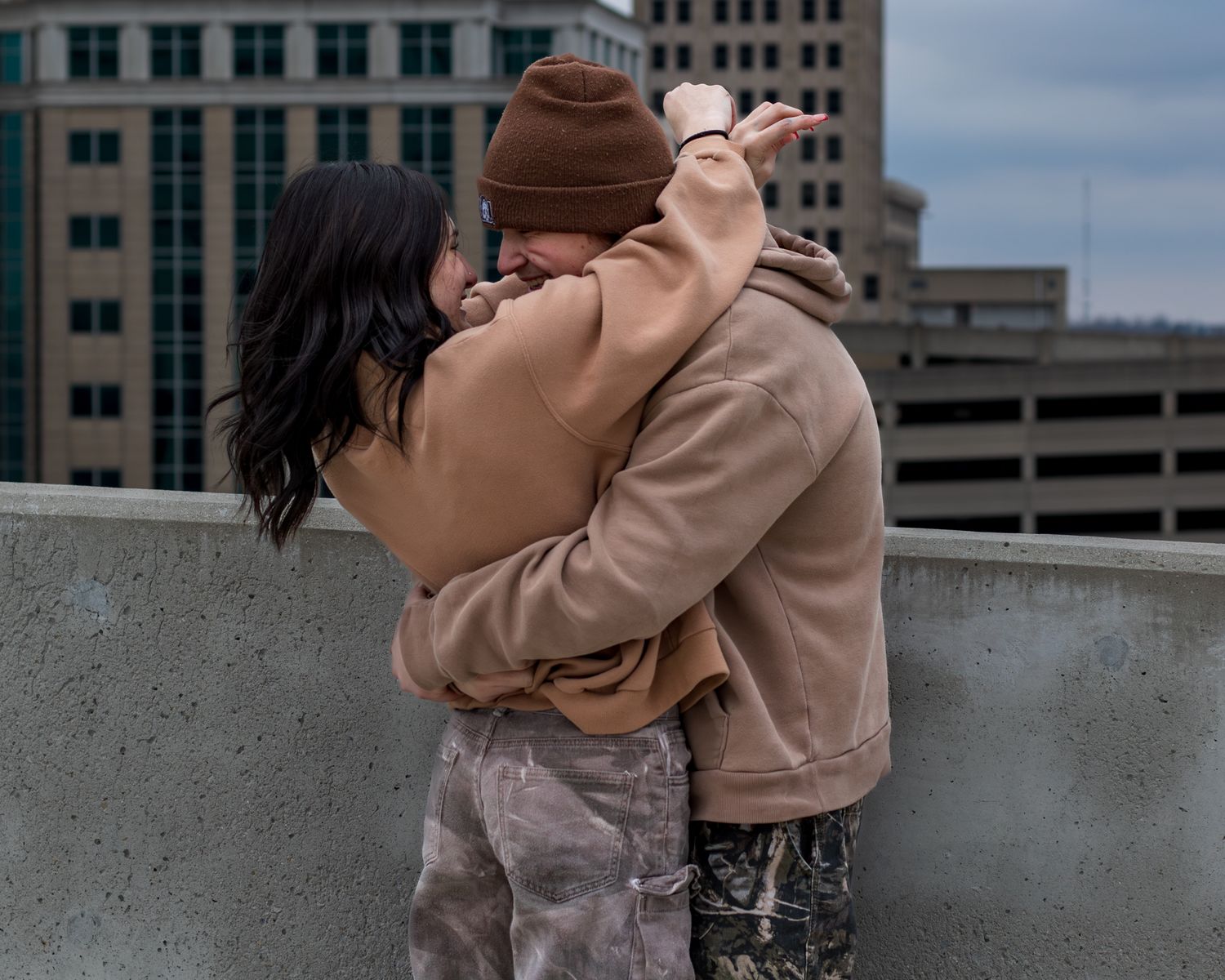 Romantic couple in neutral tones sharing an intimate moment against city backdrop.