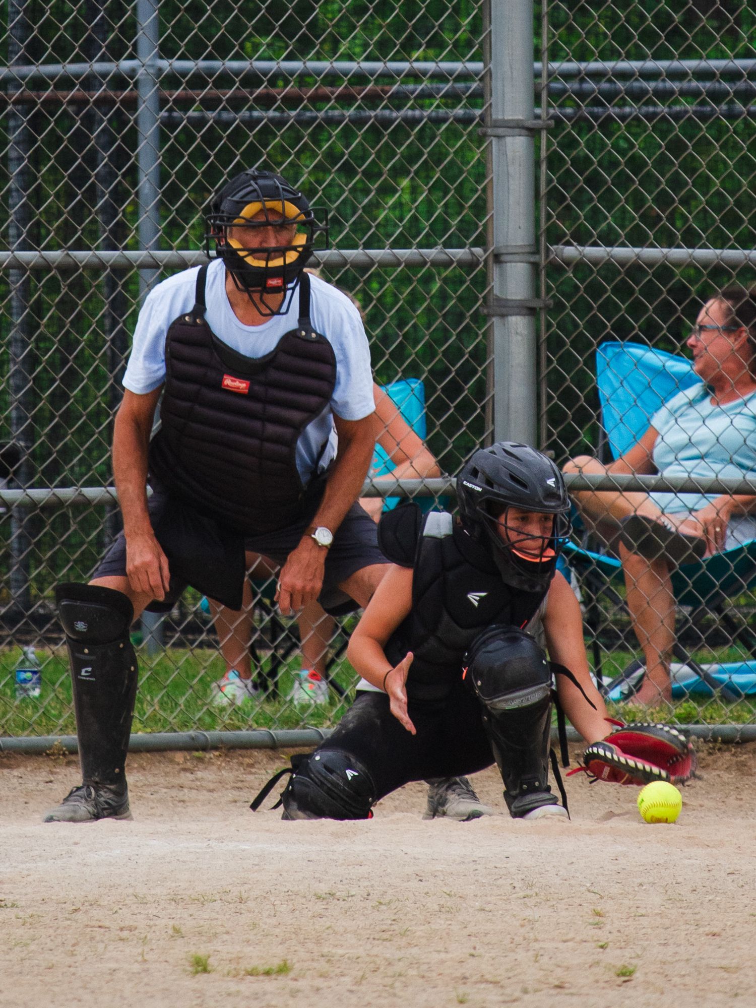 Low angle view of softball game showing catcher and umpire with spectators in background.