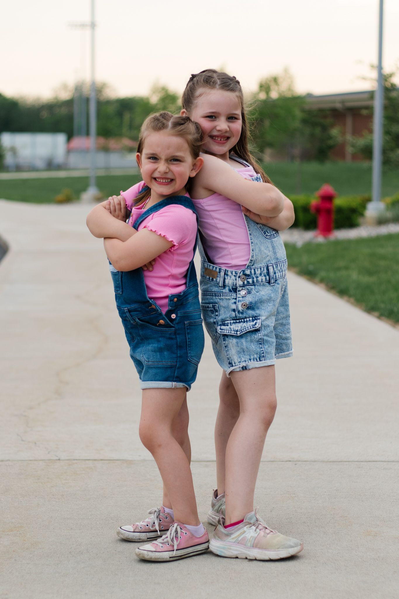Two children in denim outfits and pink shirts playing together on a sidewalk.