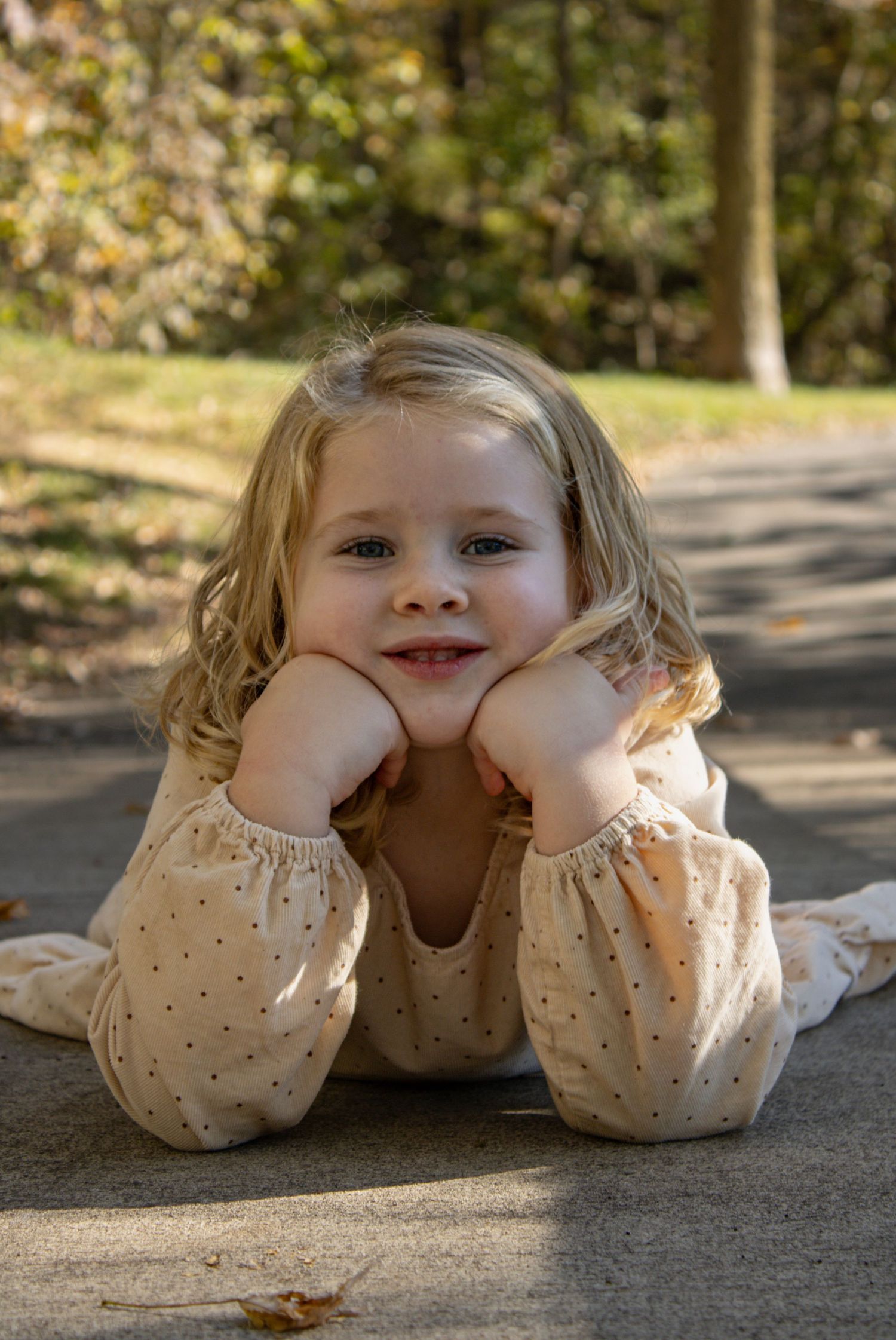 A person in a cream polka dot dress makes playful expressions while lying on concrete.