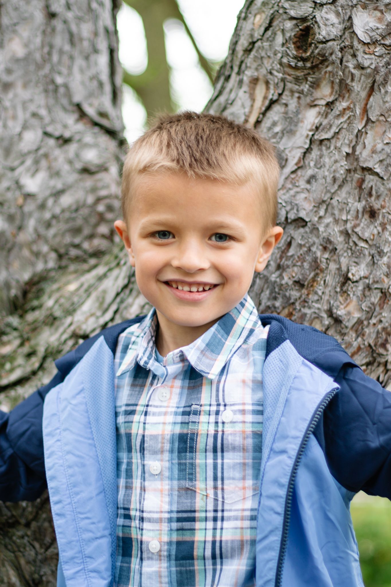 Cheerful outdoor portraits wearing casual blue layers against textured tree bark.