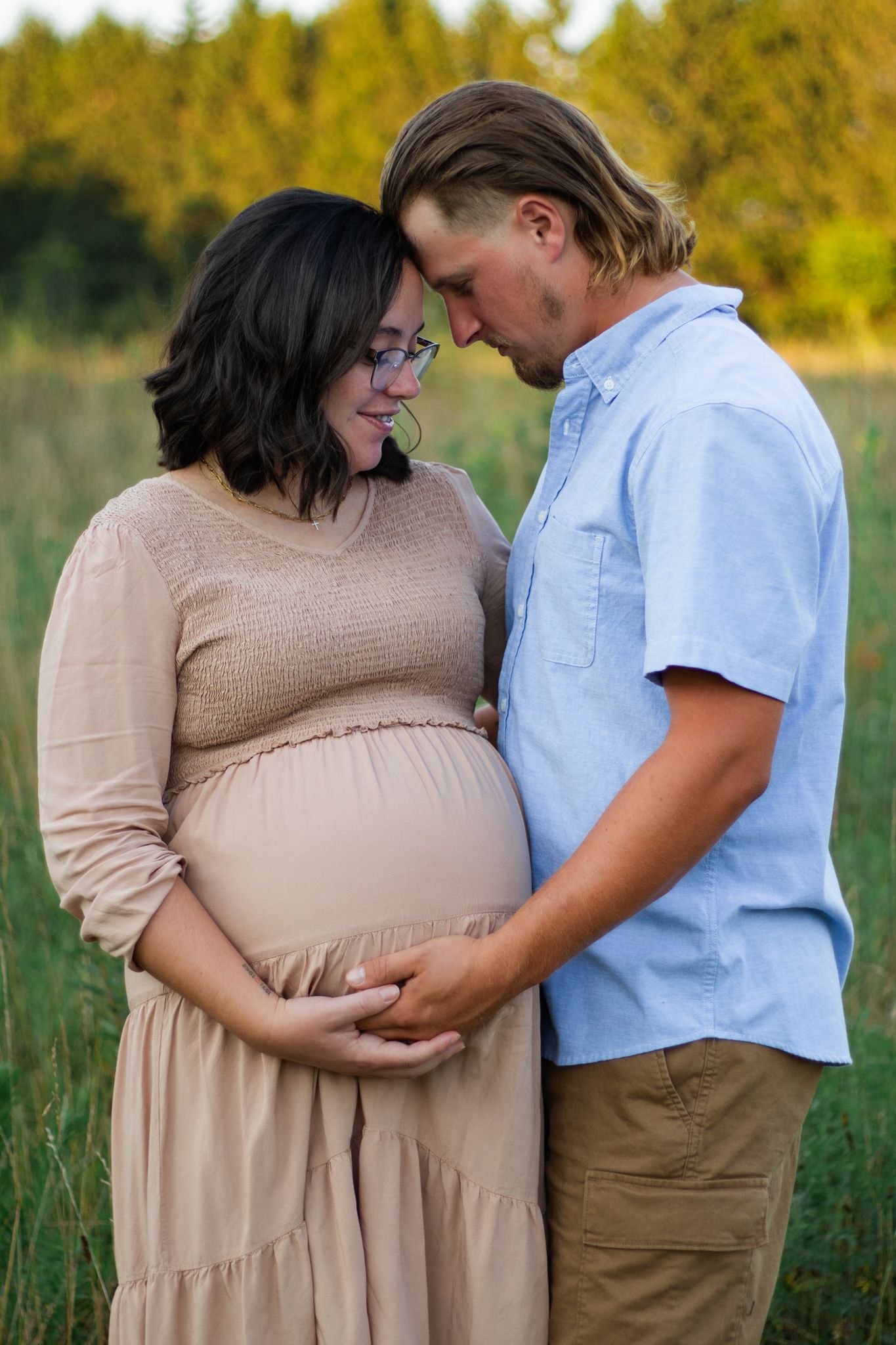 Tender maternity photography session in field during sunset.