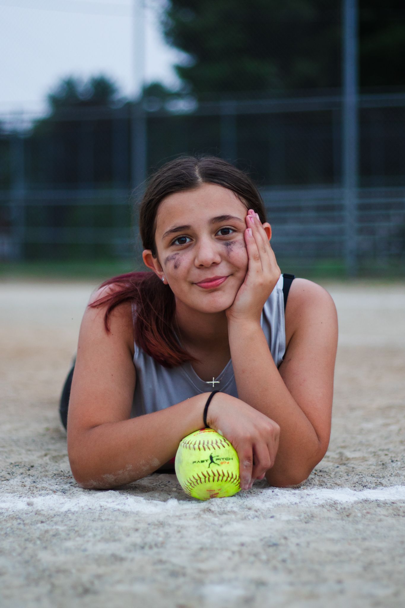 Player resting on dirt infield with bright yellow softball and casual pose during game break.