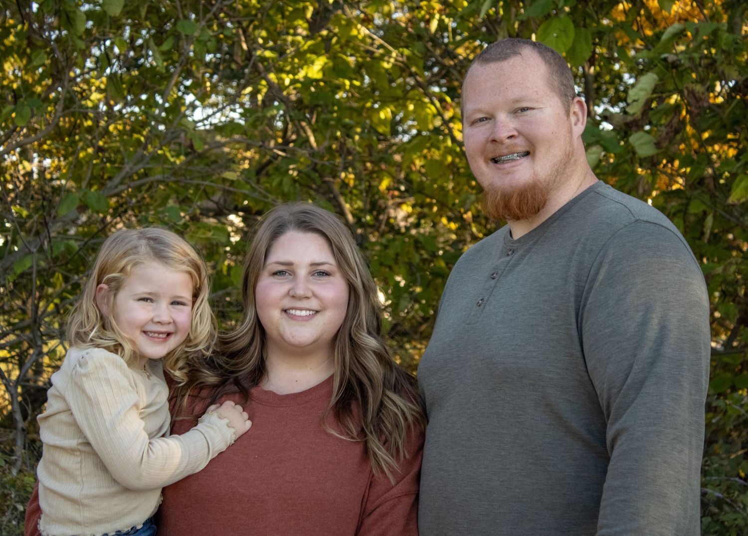 Family poses together outdoors with golden autumn foliage in the background.