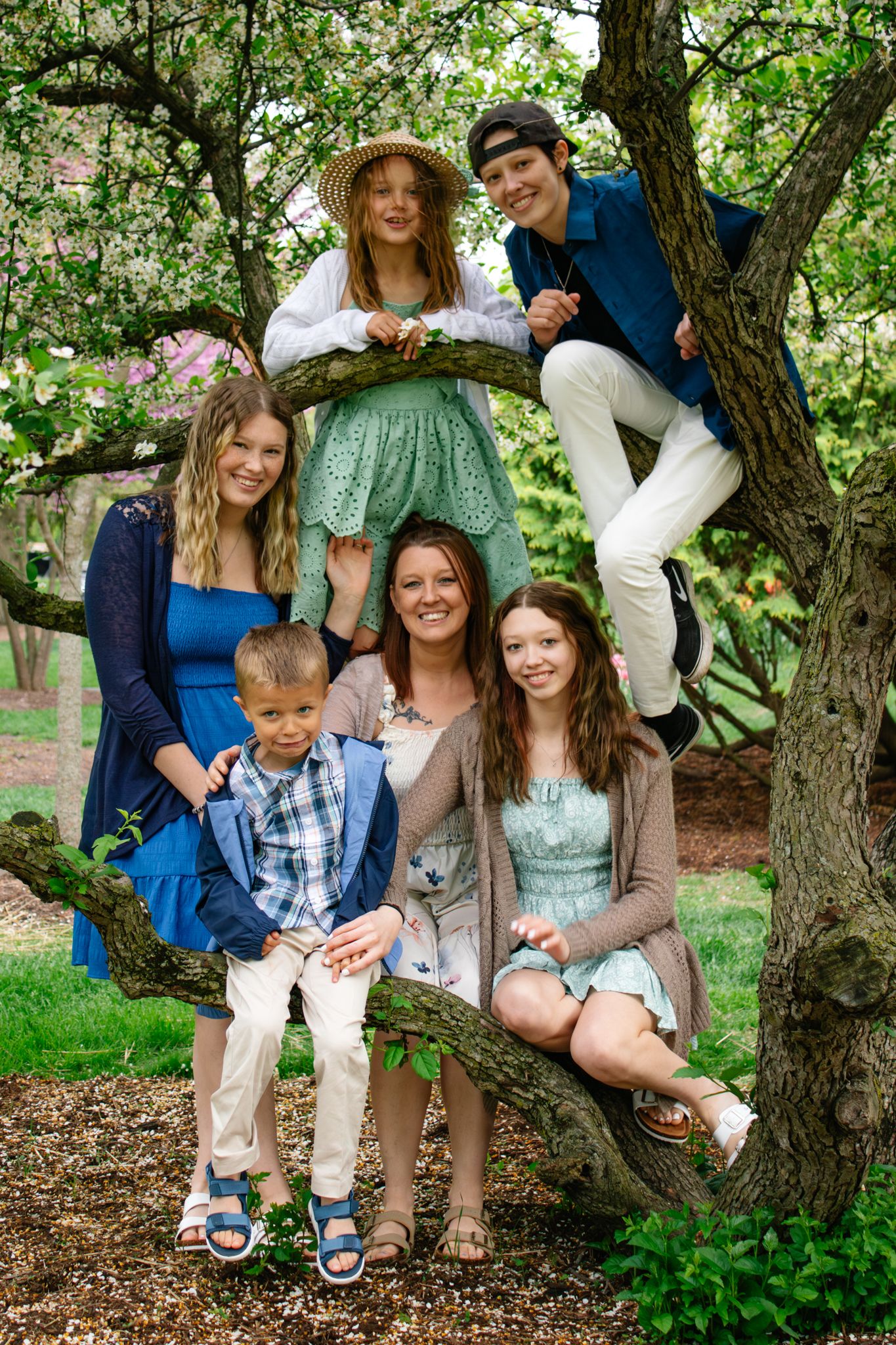 Family members gathered around a tree trunk for a casual outdoor portrait session.
