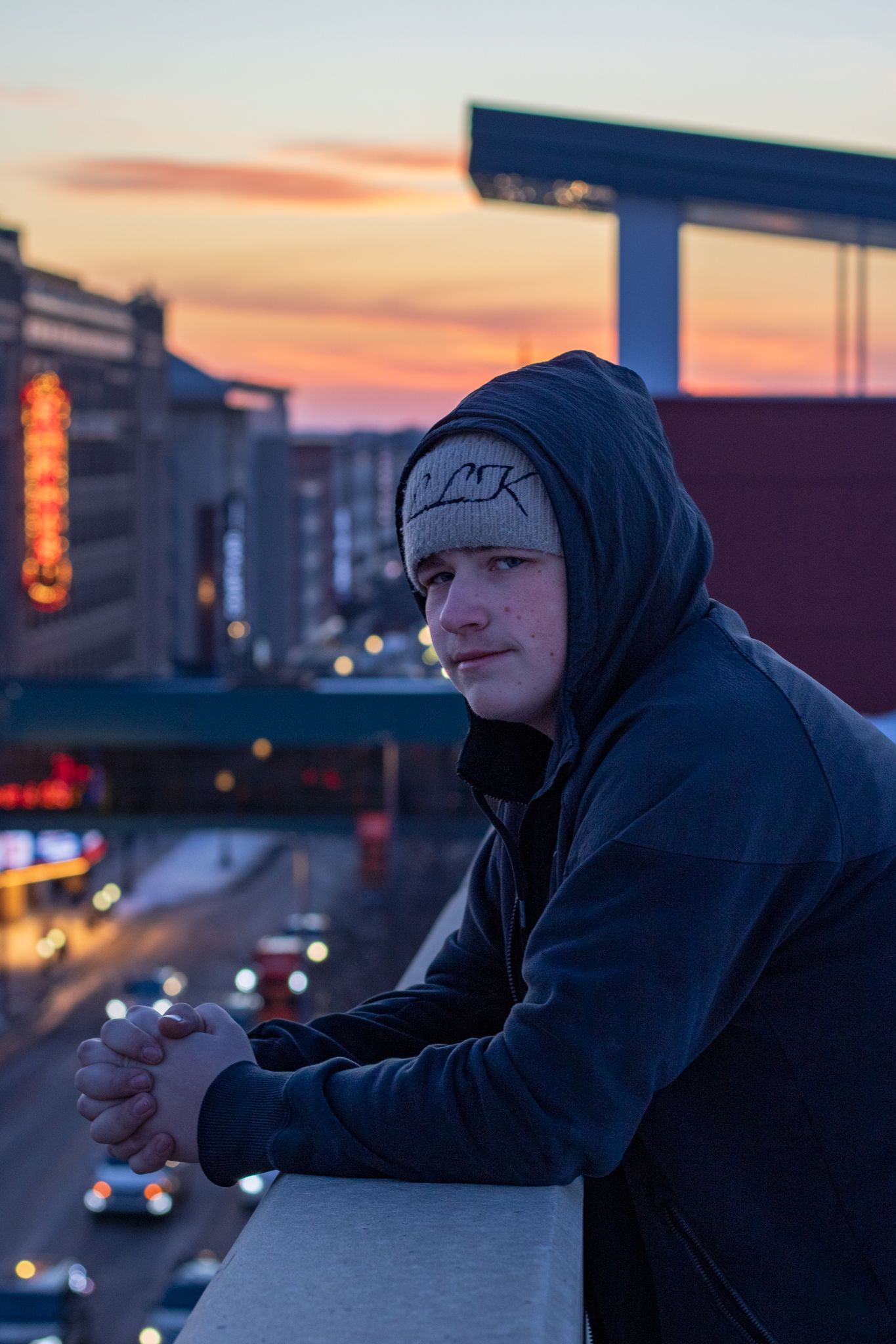 Silhouette of person against sunset sky with city lights in background.