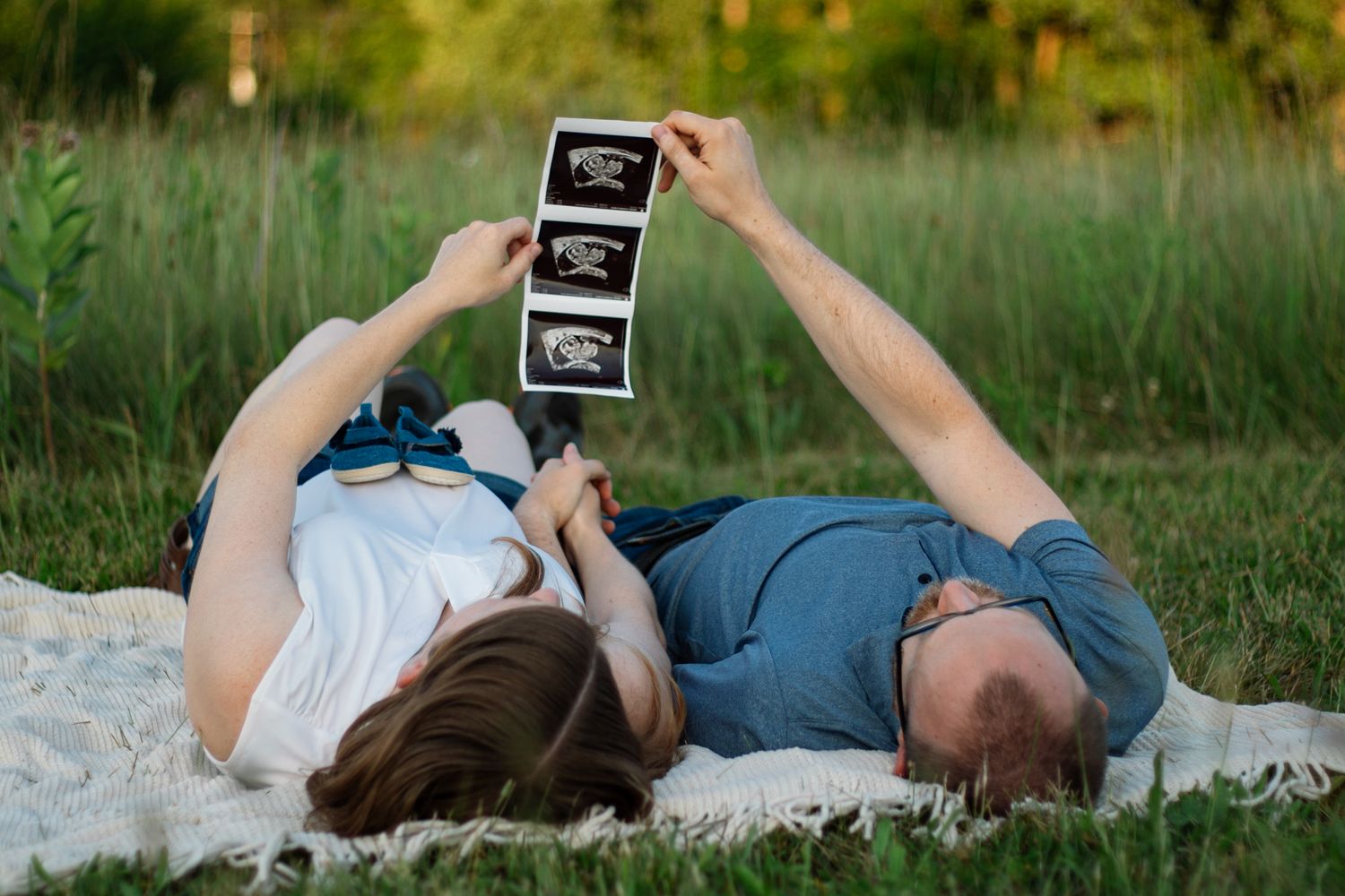Pregnancy announcement photoshoot with ultrasound pictures in natural outdoor setting.