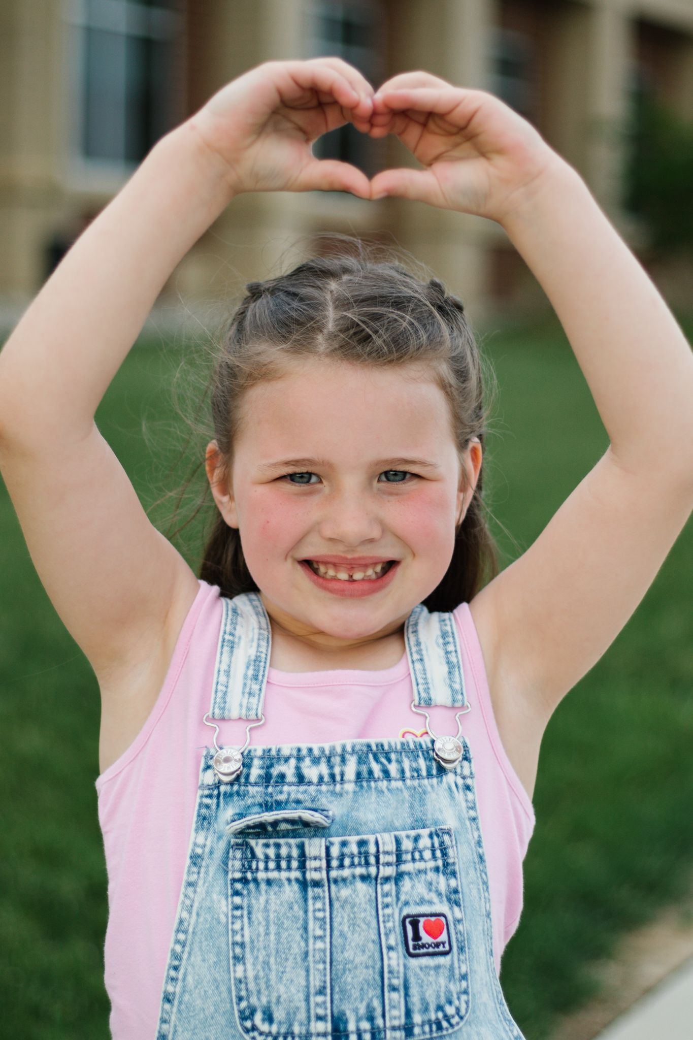 Playful sequence showing child in denim overalls and pink shirt making silly poses outdoors on grass.