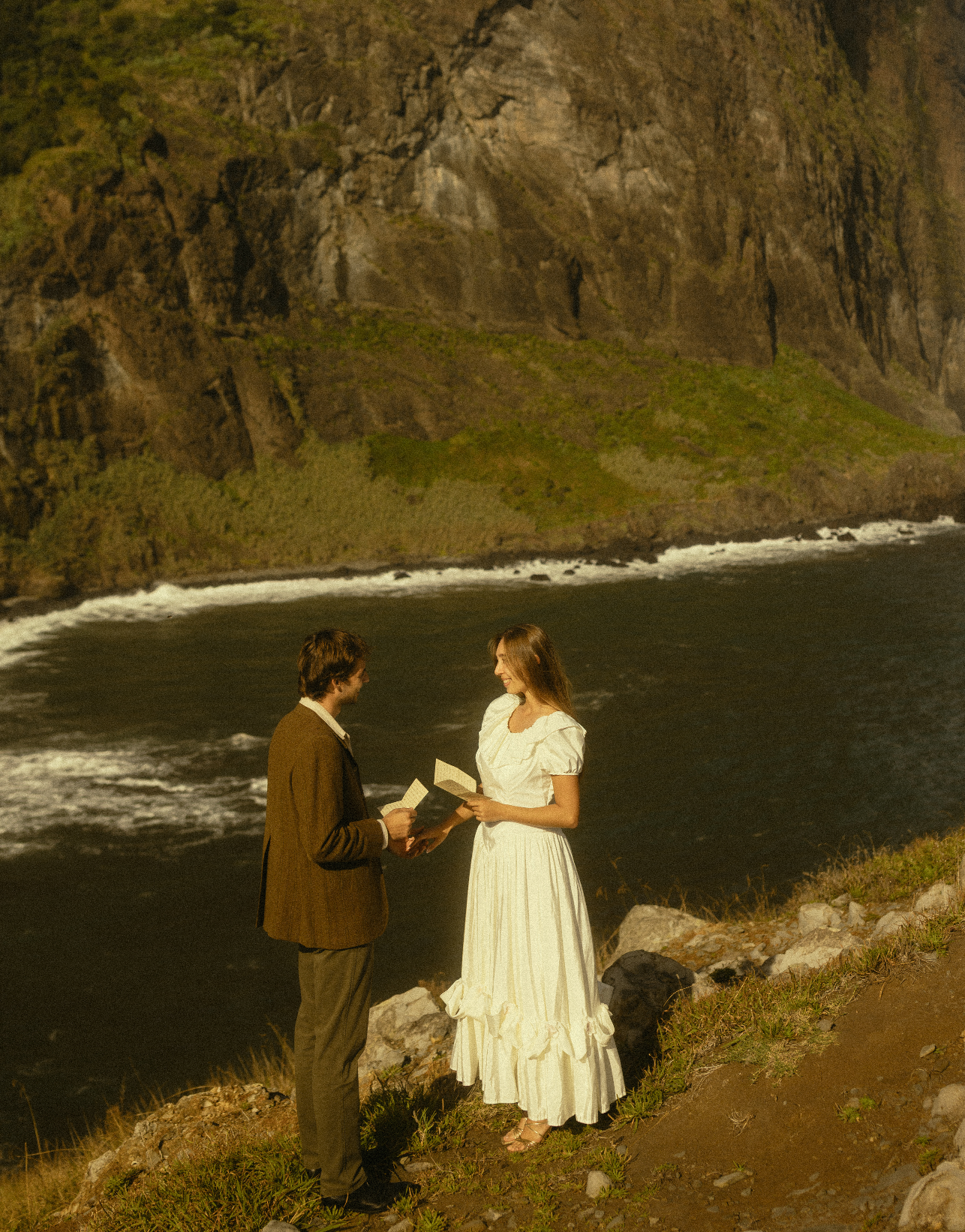 A romantic proposal scene unfolds on a dramatic coastal cliff overlooking dark waters and rugged terrain.