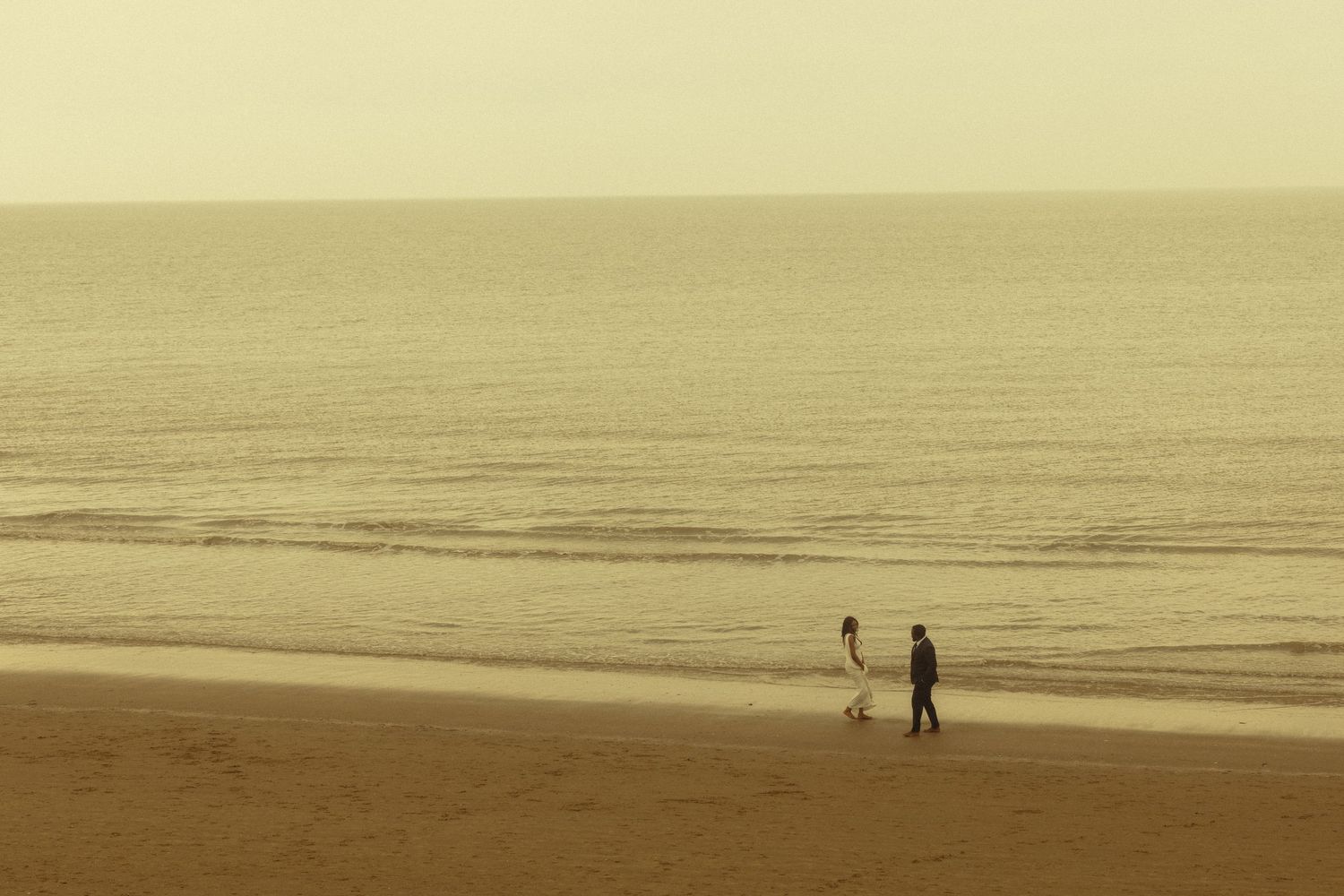 Two silhouettes walk along a misty beach at sunset creating a peaceful and serene coastal scene.
