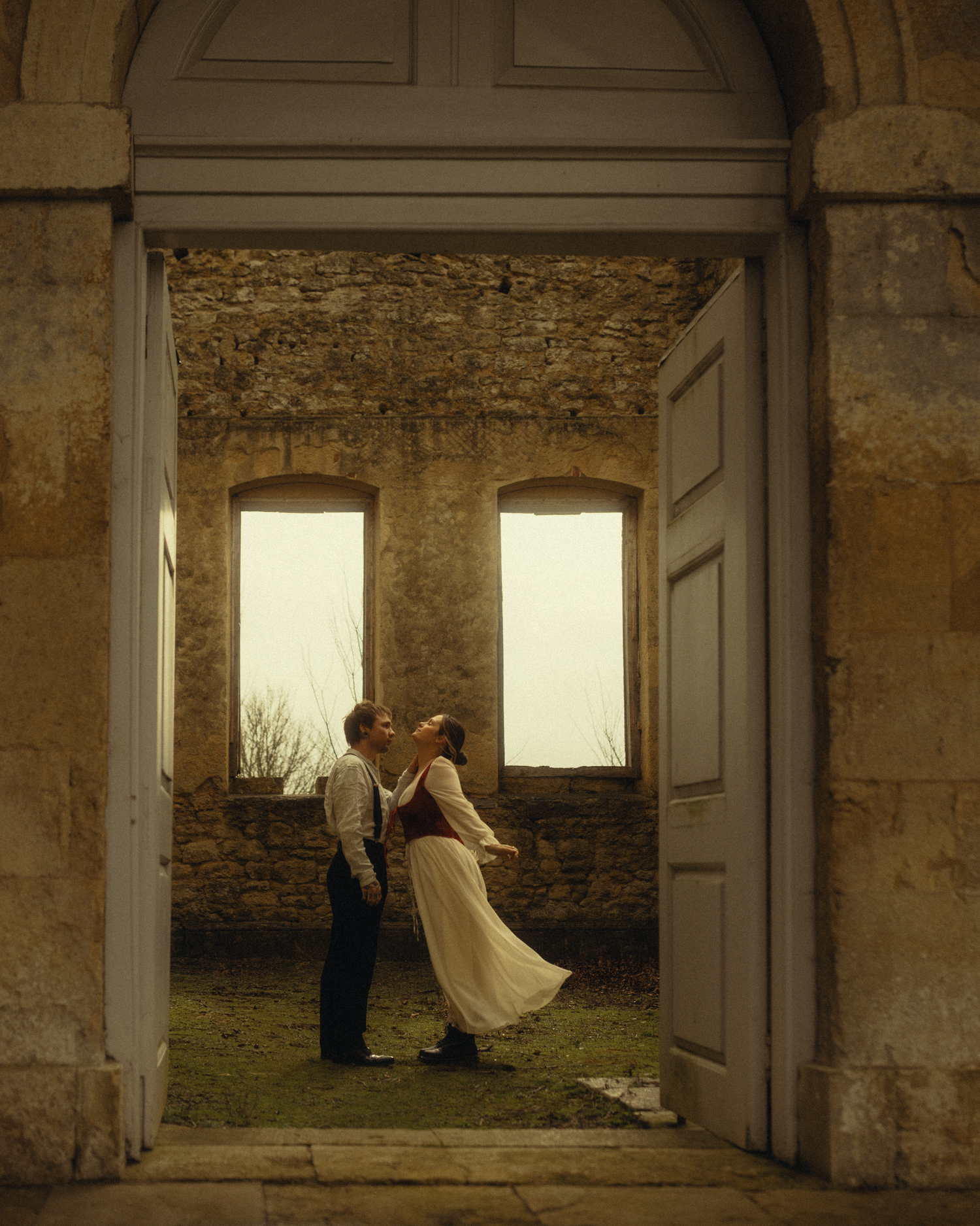 A ghostly figure in white moves through an abandoned stone room with sunlit windows creating an ethereal atmosphere.