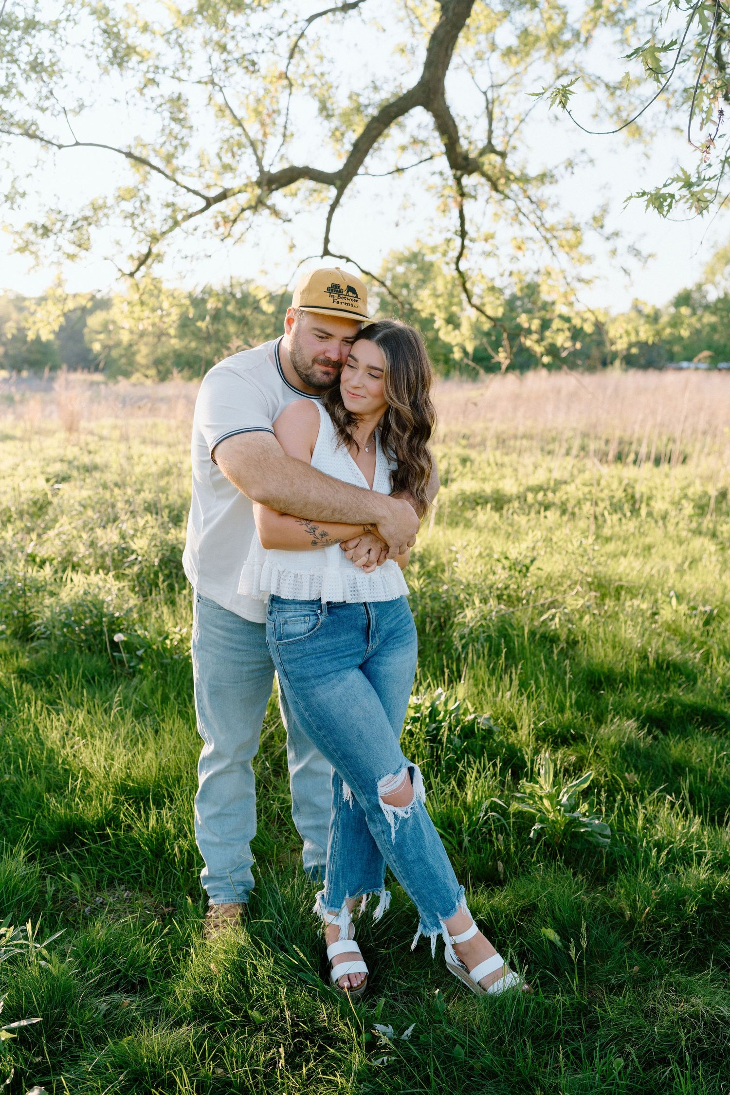 Playful couple in casual wear sharing a tender moment in a sunlit grassy field.