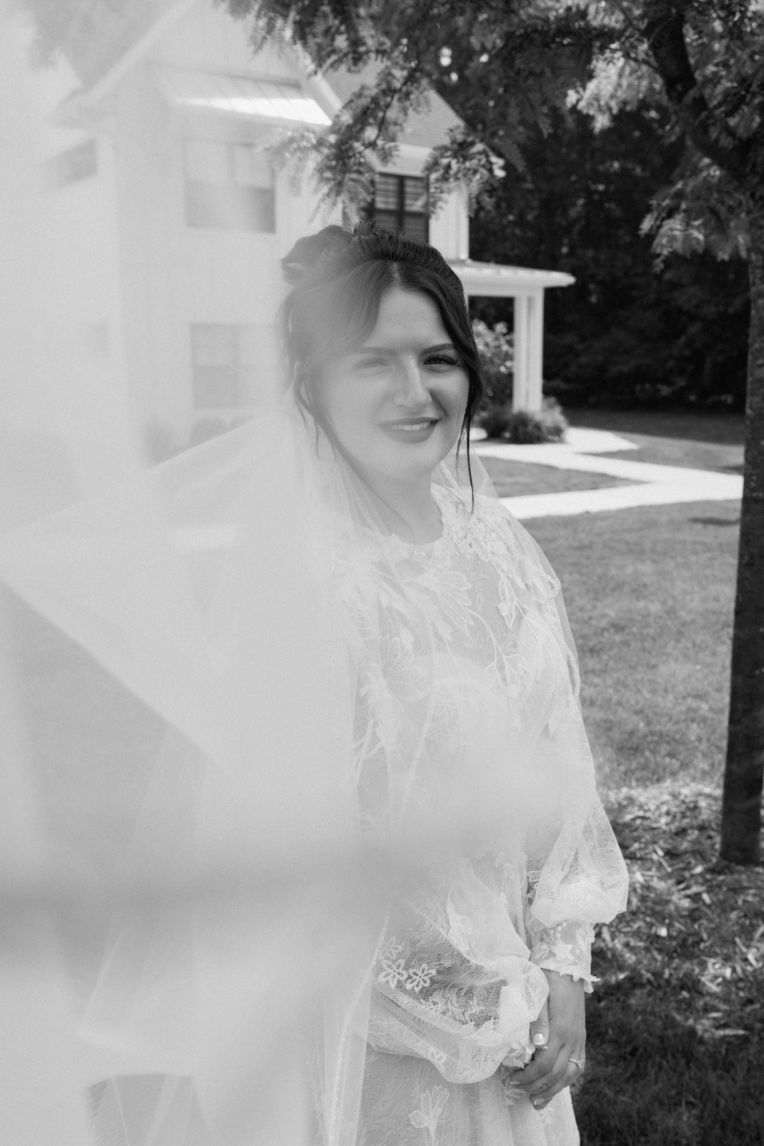 Dreamy black and white bridal portraits showing flowing lace gown details in natural outdoor setting.