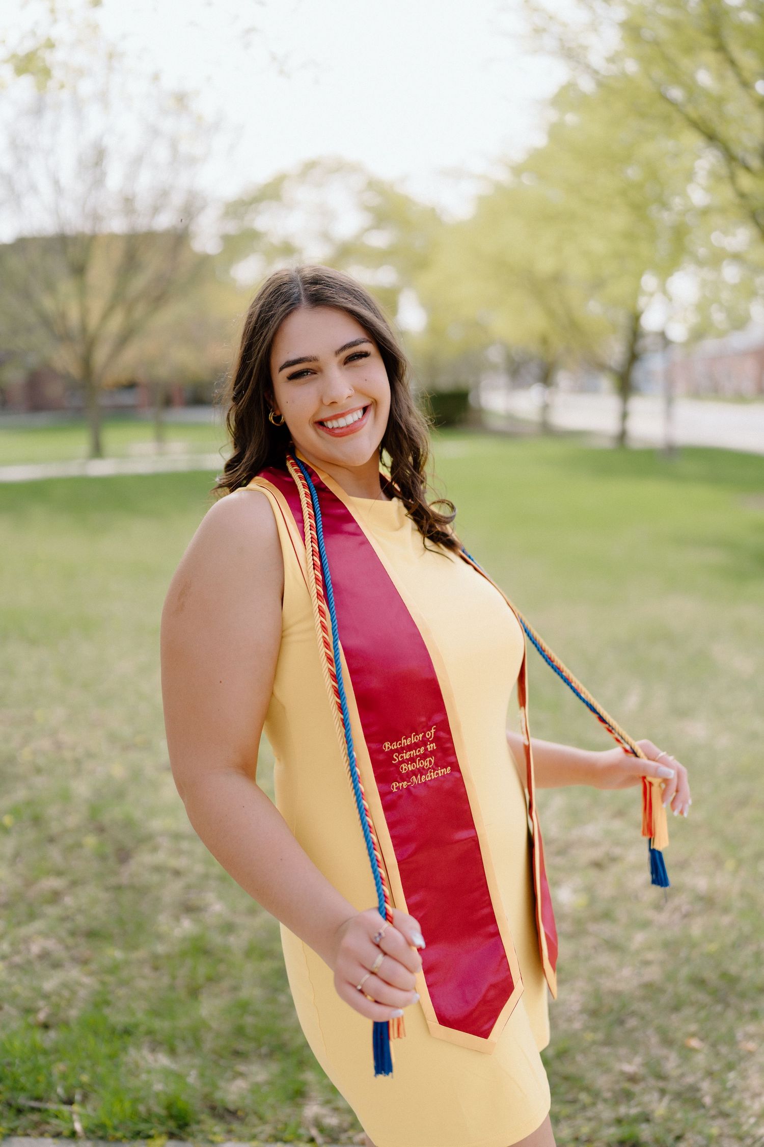 Outdoor graduation photos featuring yellow stole with red accent sash and colorful tassels.