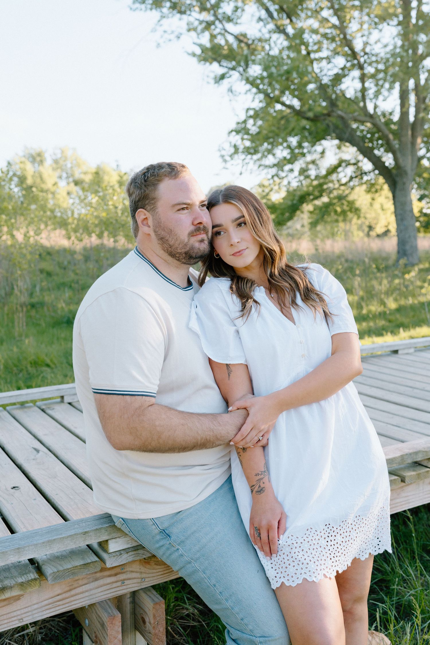 Couple in white sits together intimately on a wooden deck surrounded by green grass.
