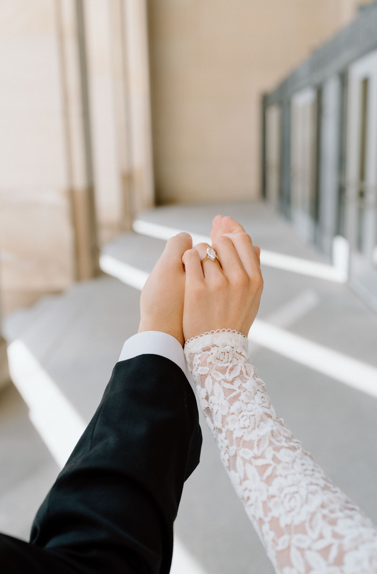 Close-up view of hands wearing black and white lace wedding attire showing engagement ring in natural light.