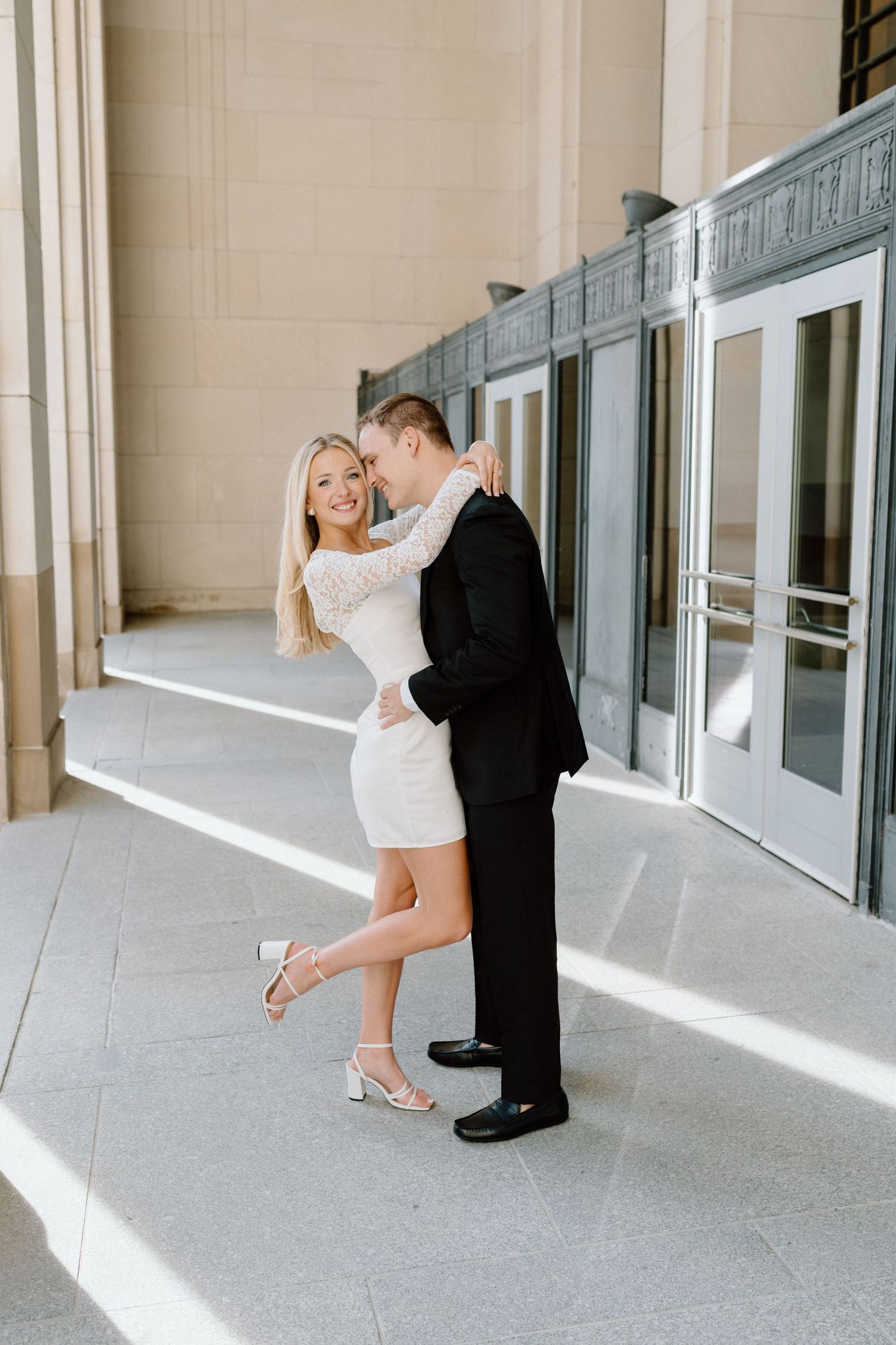A romantic couple in formal attire shares an intimate dance pose in a sunlit hallway.