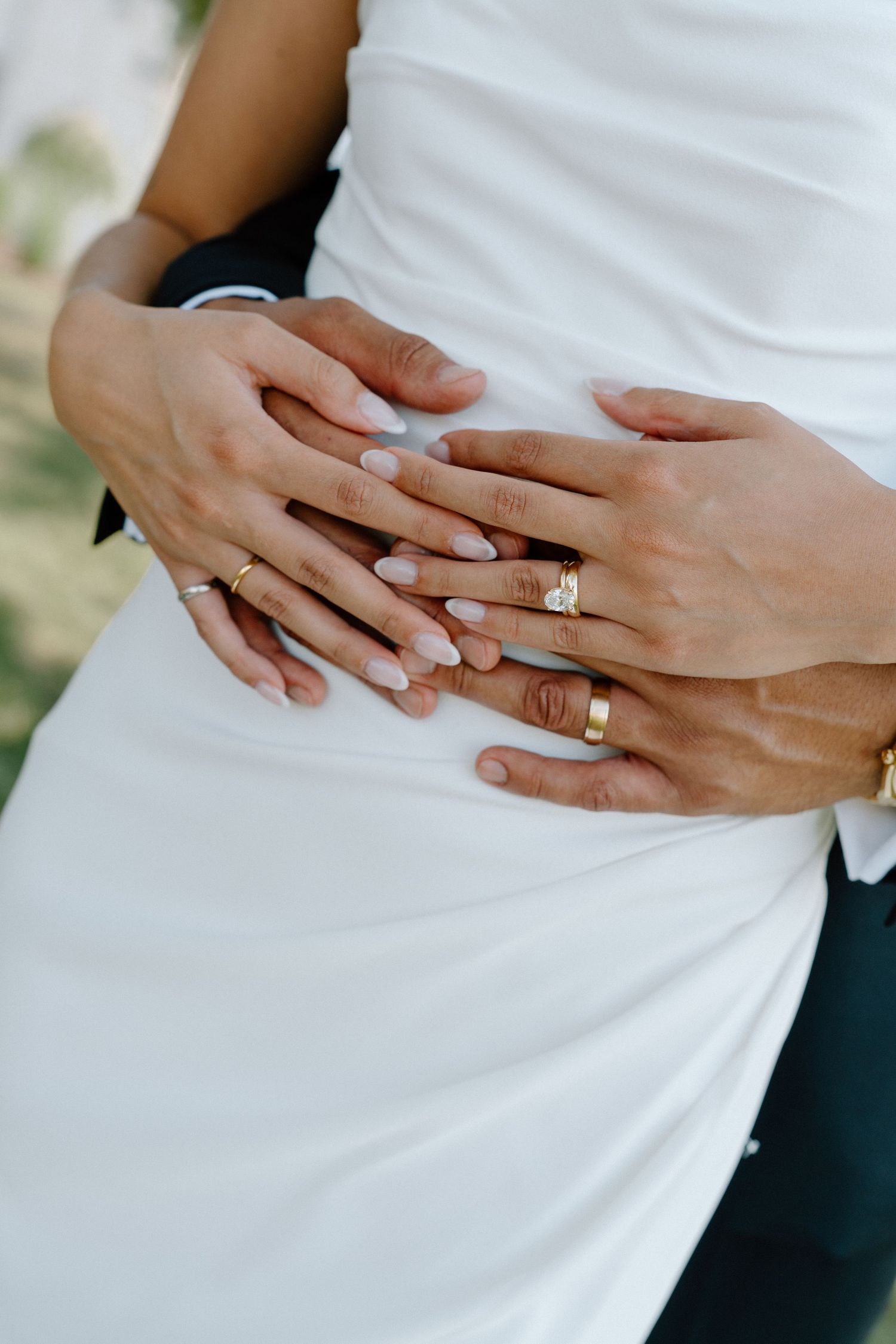 Close-up of wedding rings and hands against white fabric showing elegant diamond engagement ring and wedding bands.
