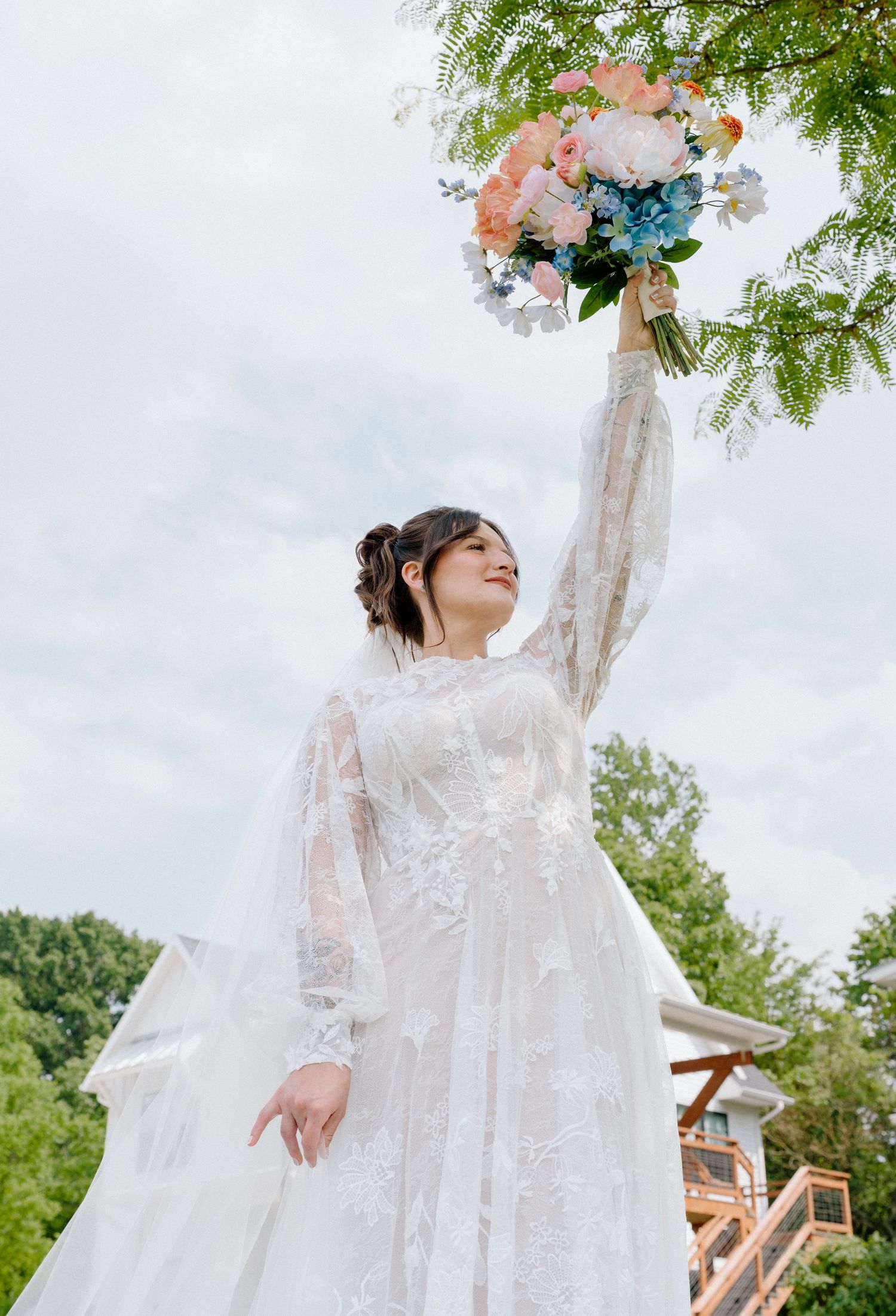 Ethereal bridal portraits showing flowing lace dress against blue sky and trees.