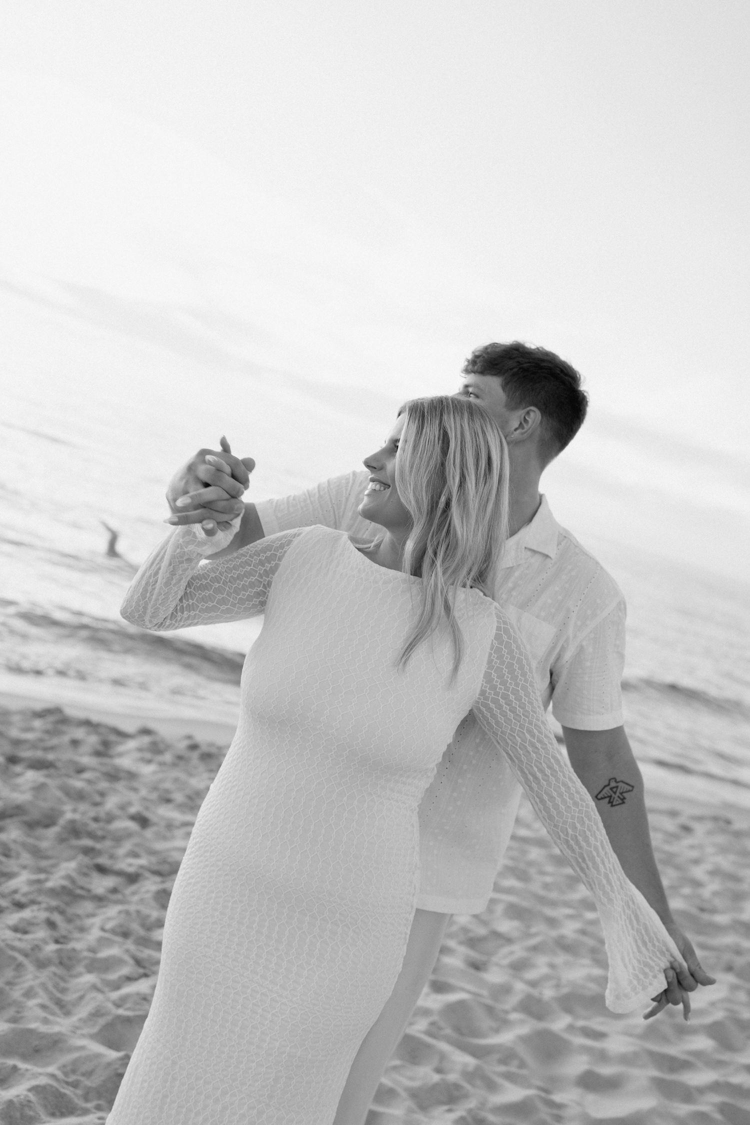 A black and white photo of a couple dancing joyfully on the beach.