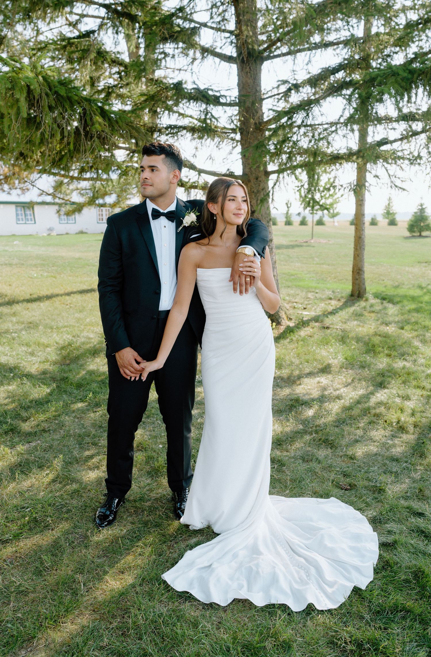 A couple poses elegantly among evergreen trees in formal wedding attire.
