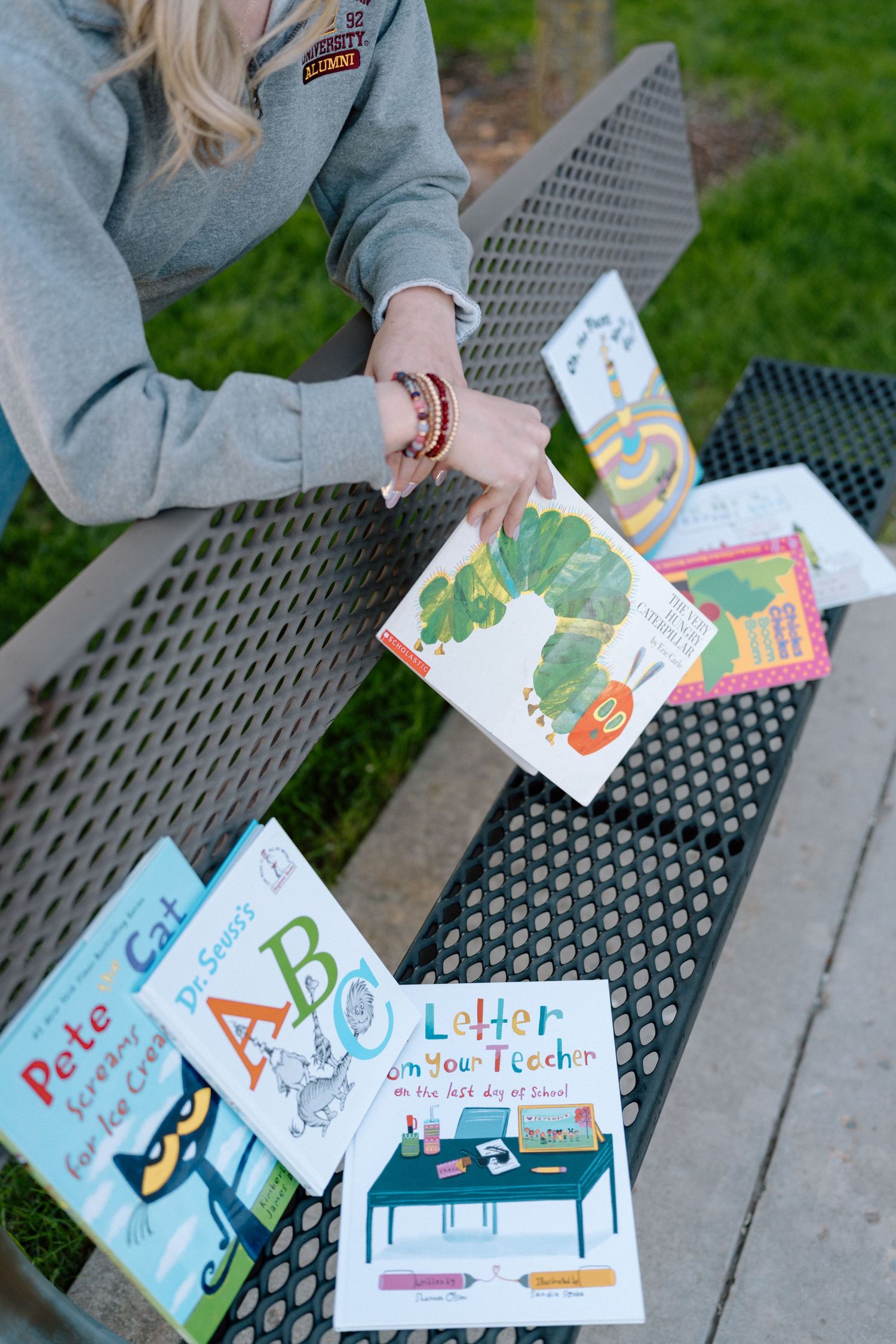 Children's educational books and learning materials spread out on metal bench outdoors.