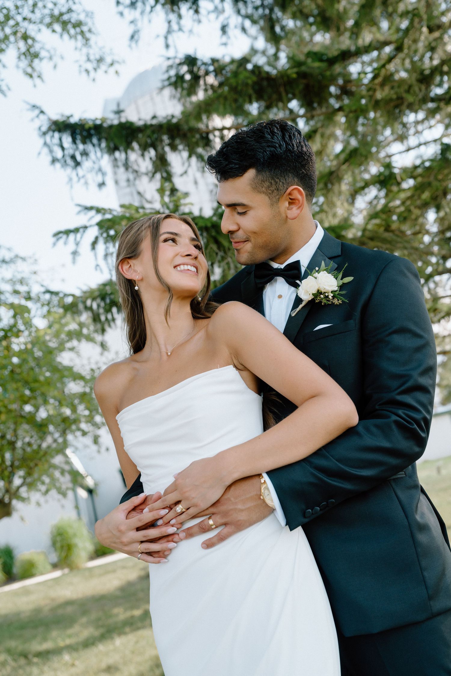 Candid wedding moment captured showing genuine laughter and embrace between newlyweds outdoors.