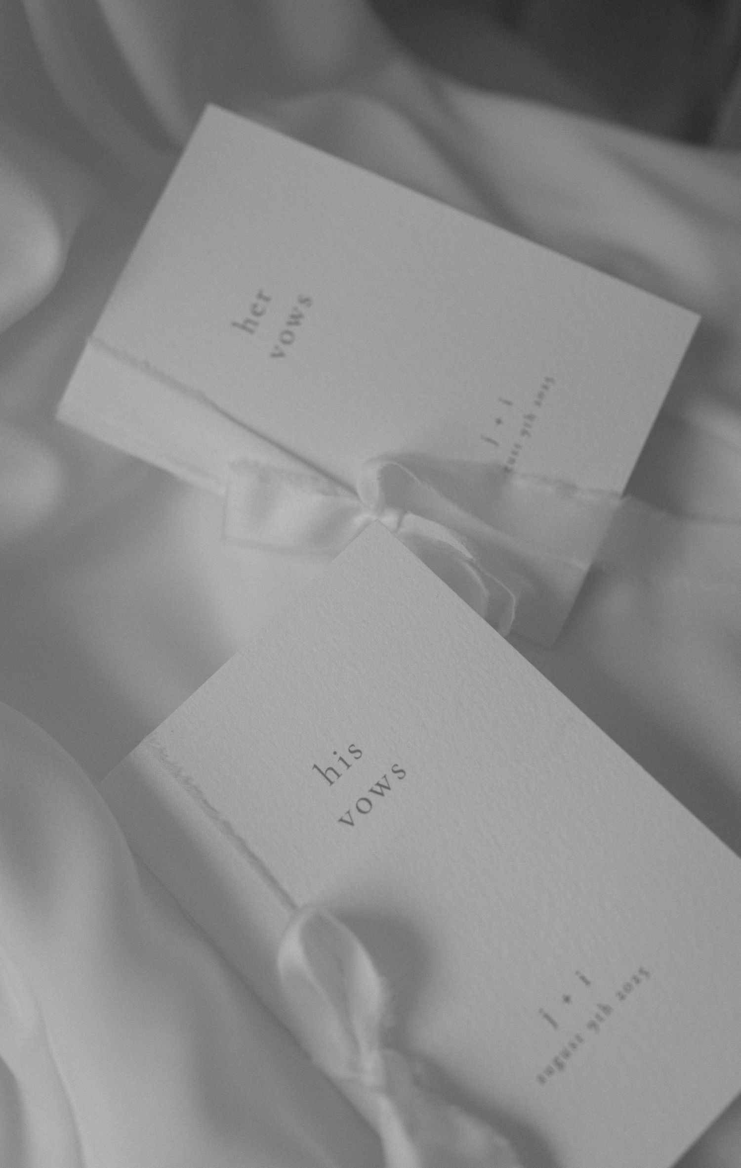 Two elegant white wedding vow books with ribbon ties on silk fabric.