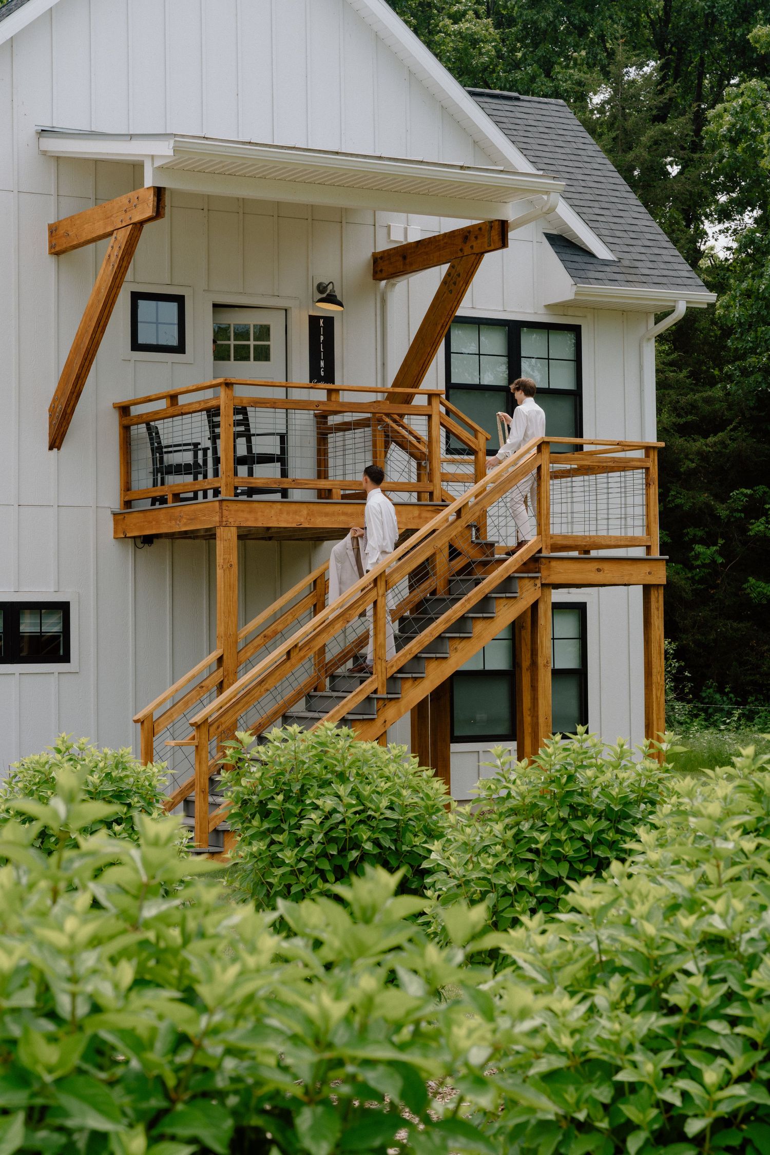 Modern white farmhouse-style venue with wooden deck railings and lush green landscaping.