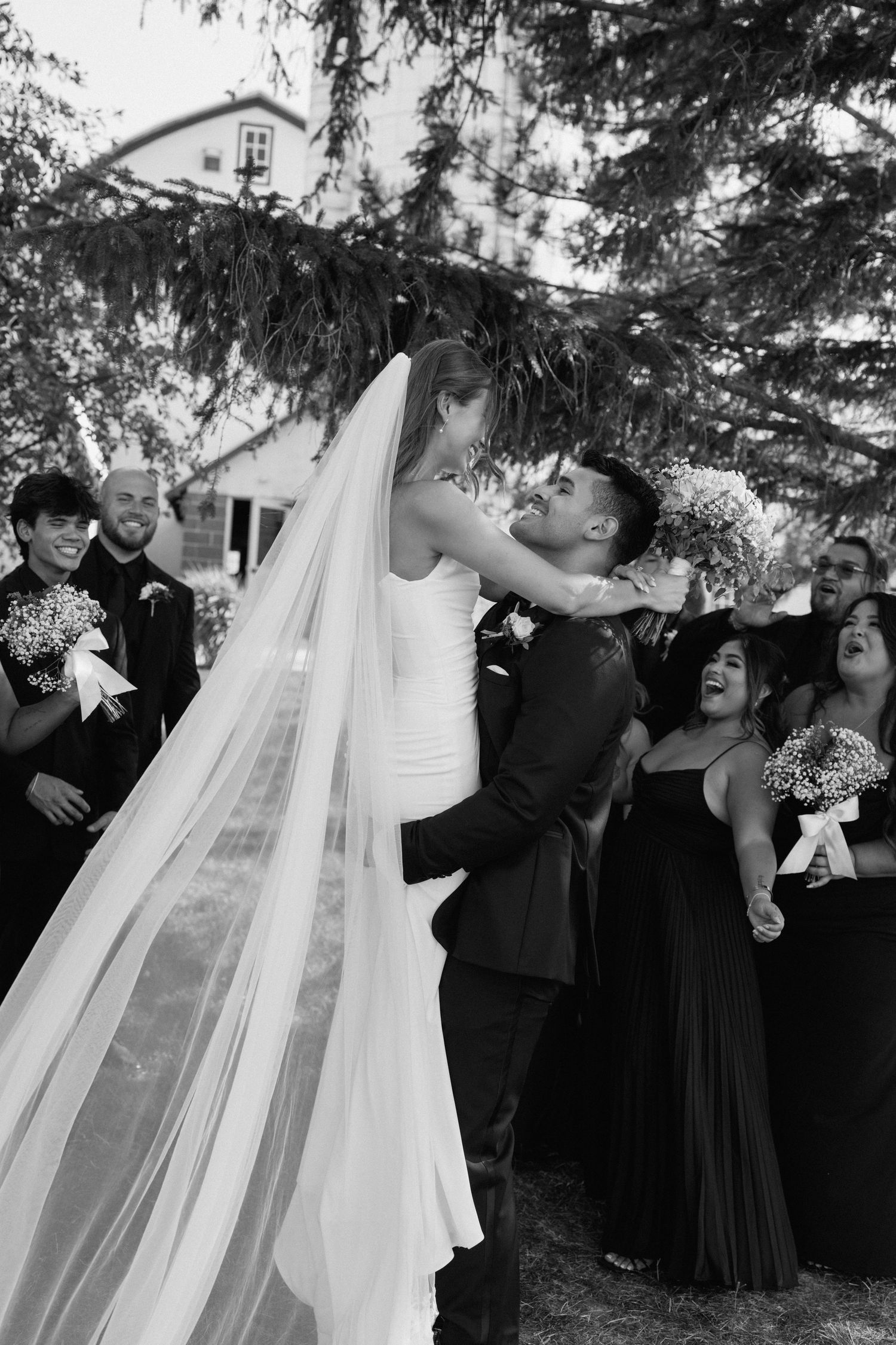 A romantic wedding moment captured in black and white under pine trees.
