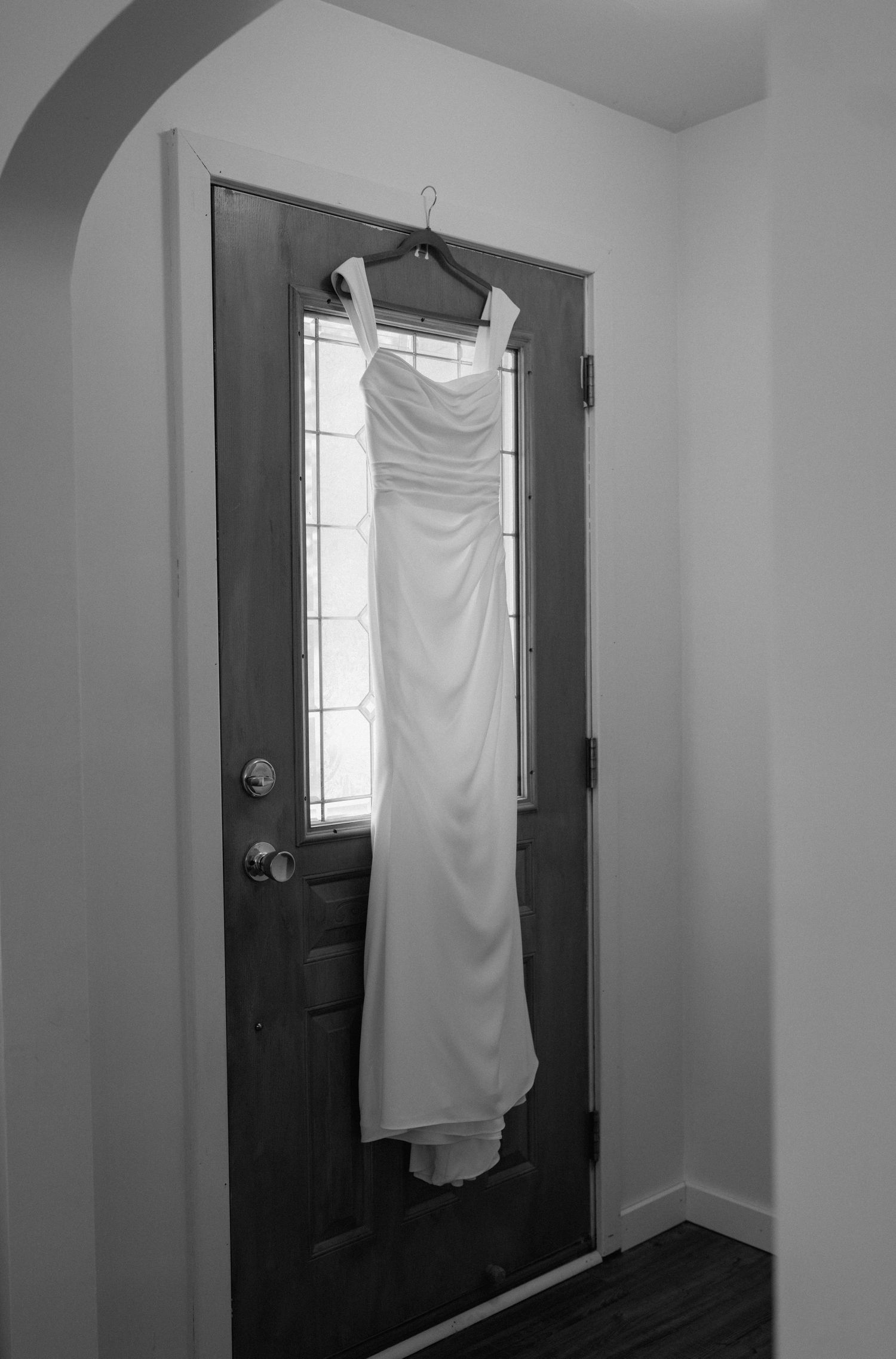 Black and white images of a white wedding dress hanging against dark doors.