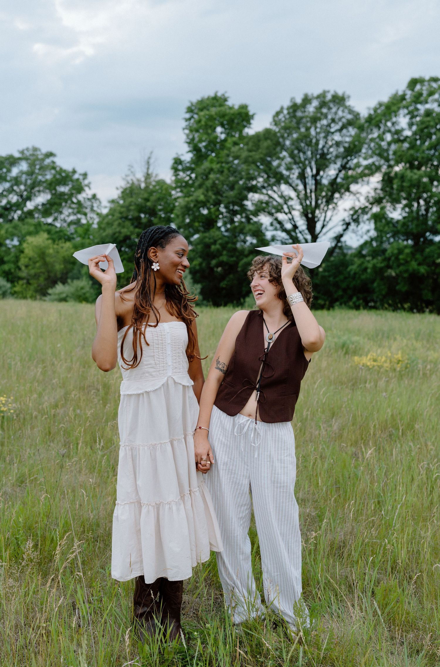 Two friends laughing and holding up paper in a grassy meadow on a summer day.