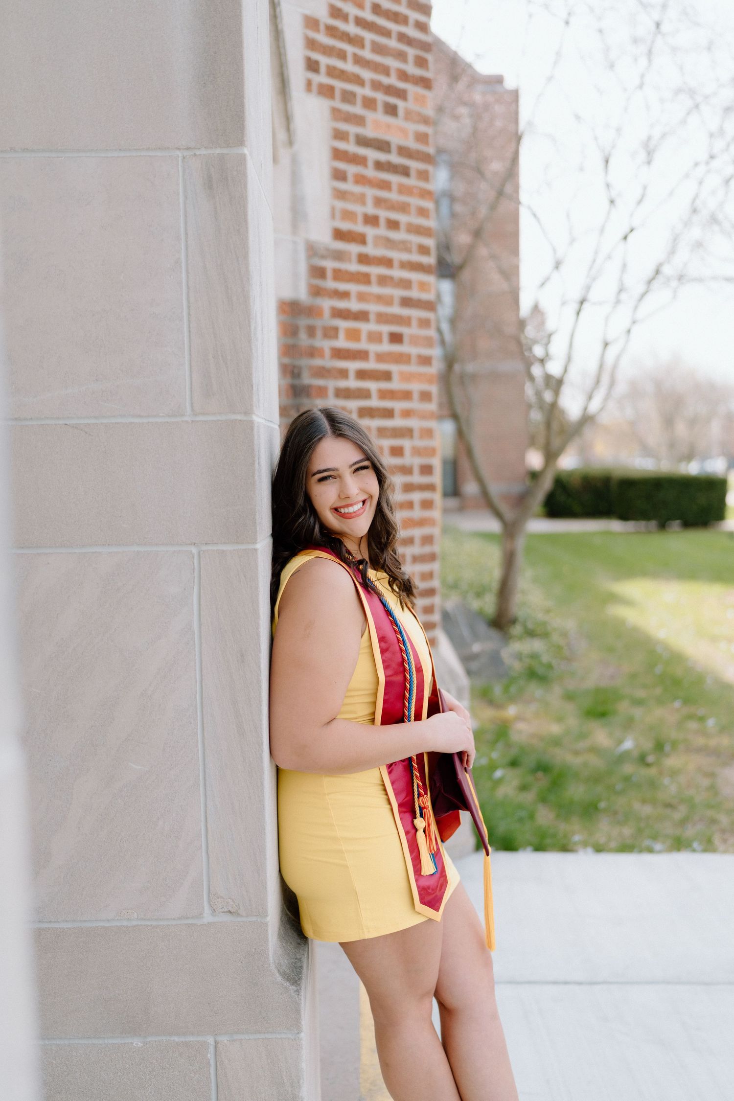 Graduation portraits in yellow stole and maroon gown taken under brick archway.