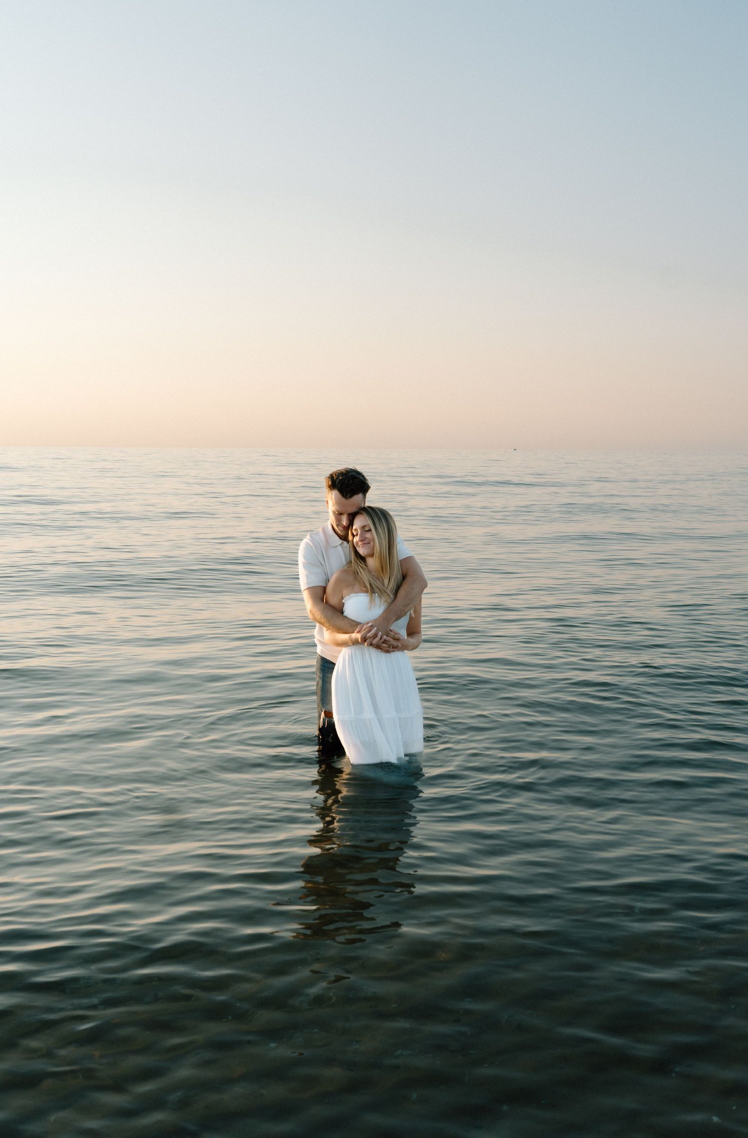 Couple embracing in calm ocean waters during sunset.