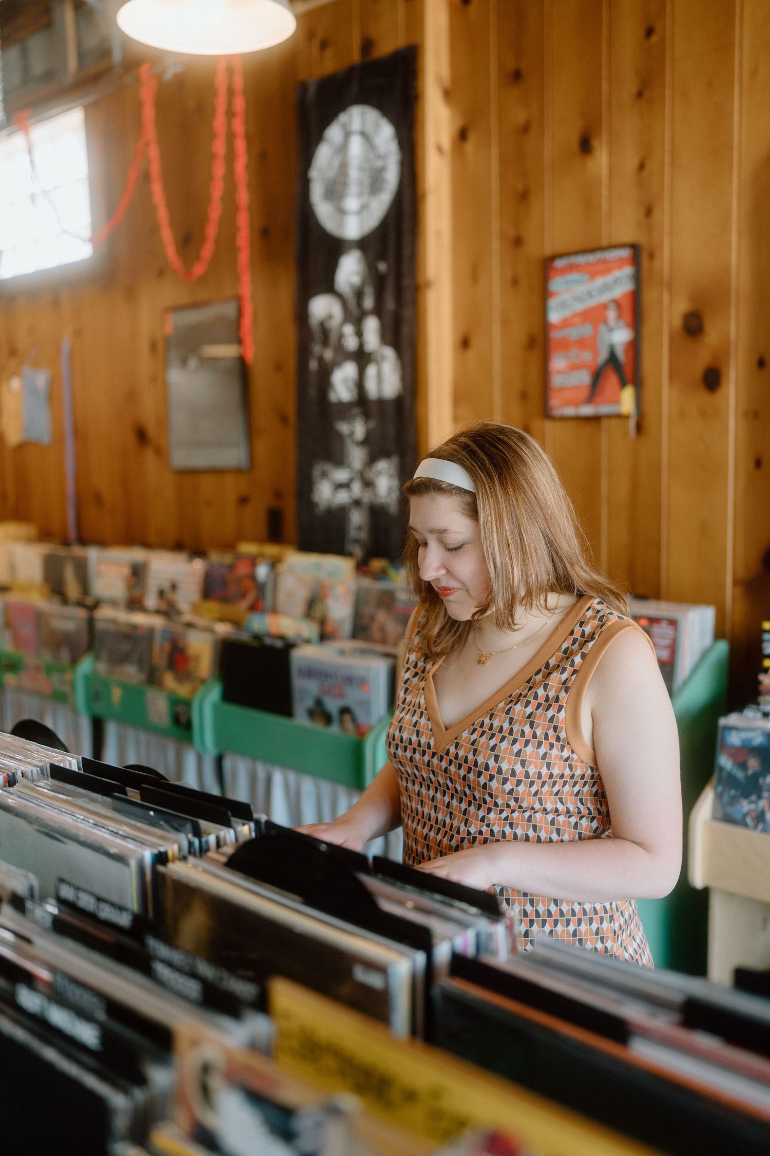 Person in a patterned dress browses through vinyl records in a wood-paneled room.