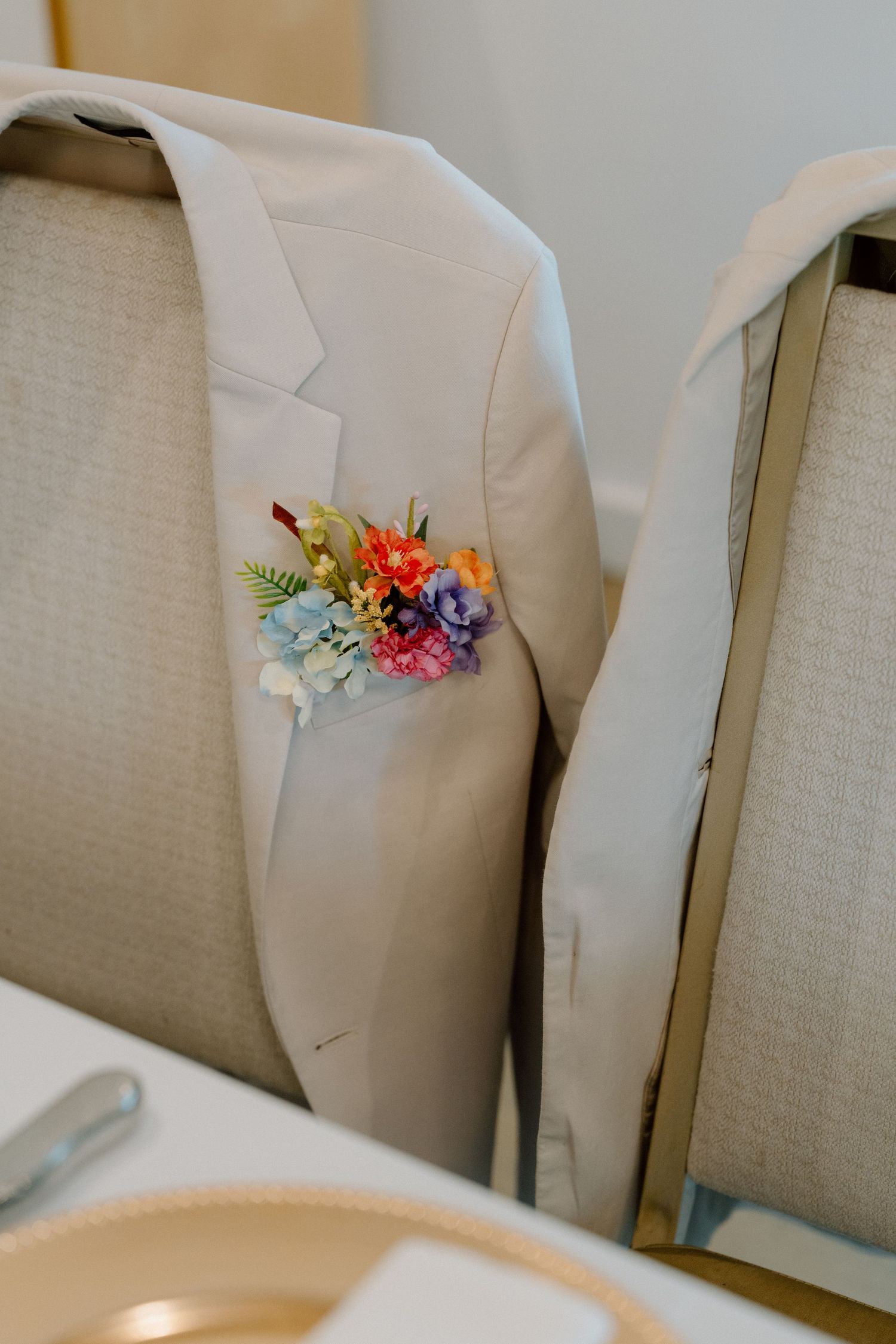 Tan suit jackets with colorful floral boutonnieres displayed on hangers.