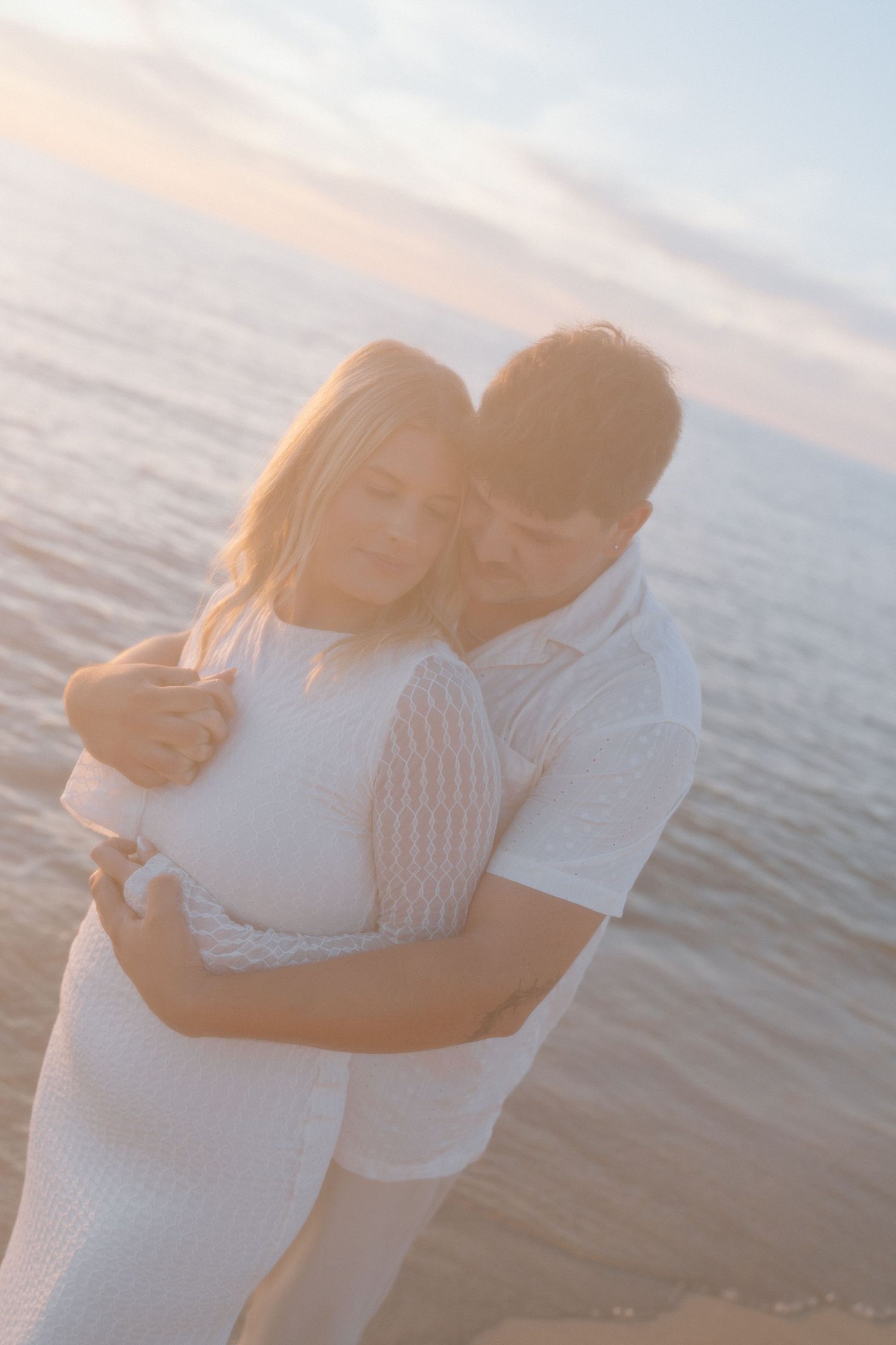 A couple embraces on the beach during golden hour sunset.