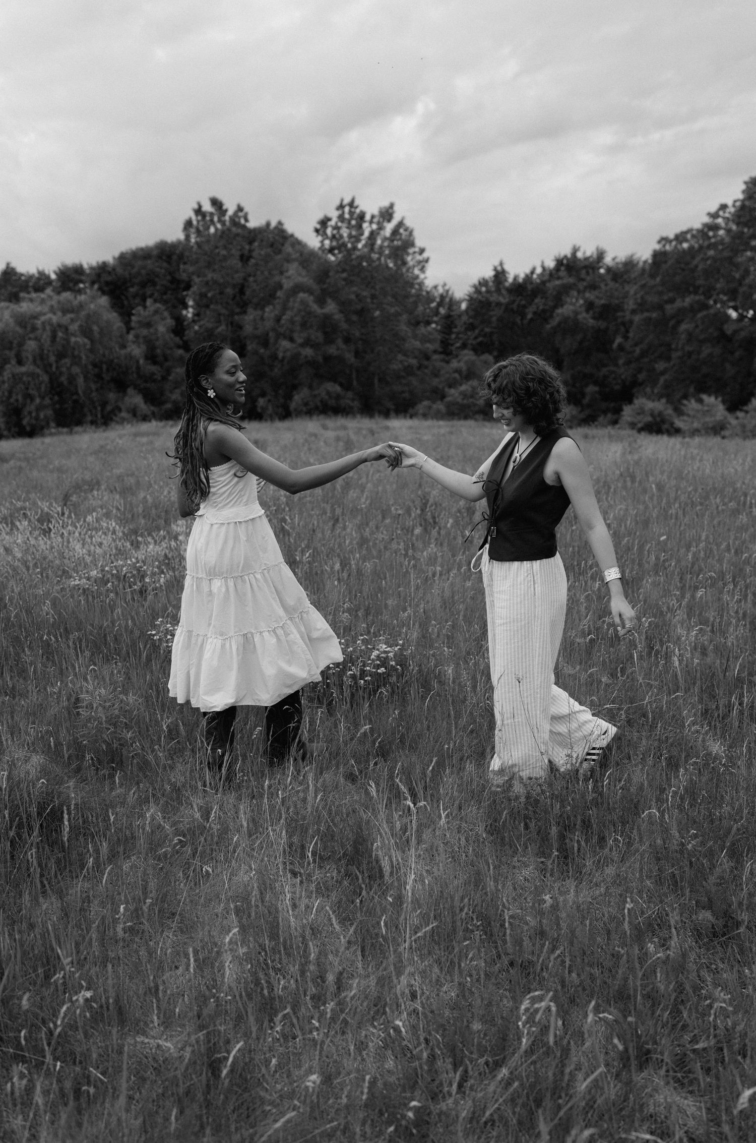 Two friends dancing together in a field with trees in the background on a cloudy day.