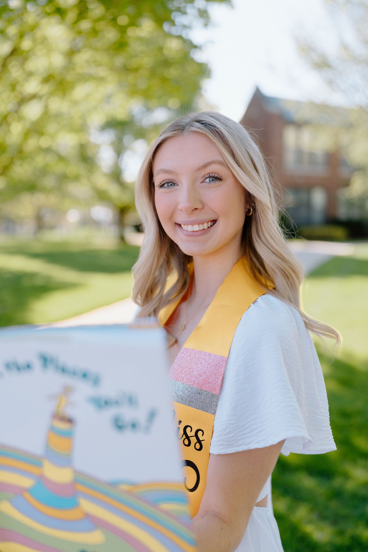 Person in white shirt displays college apparel and academic regalia outdoors.