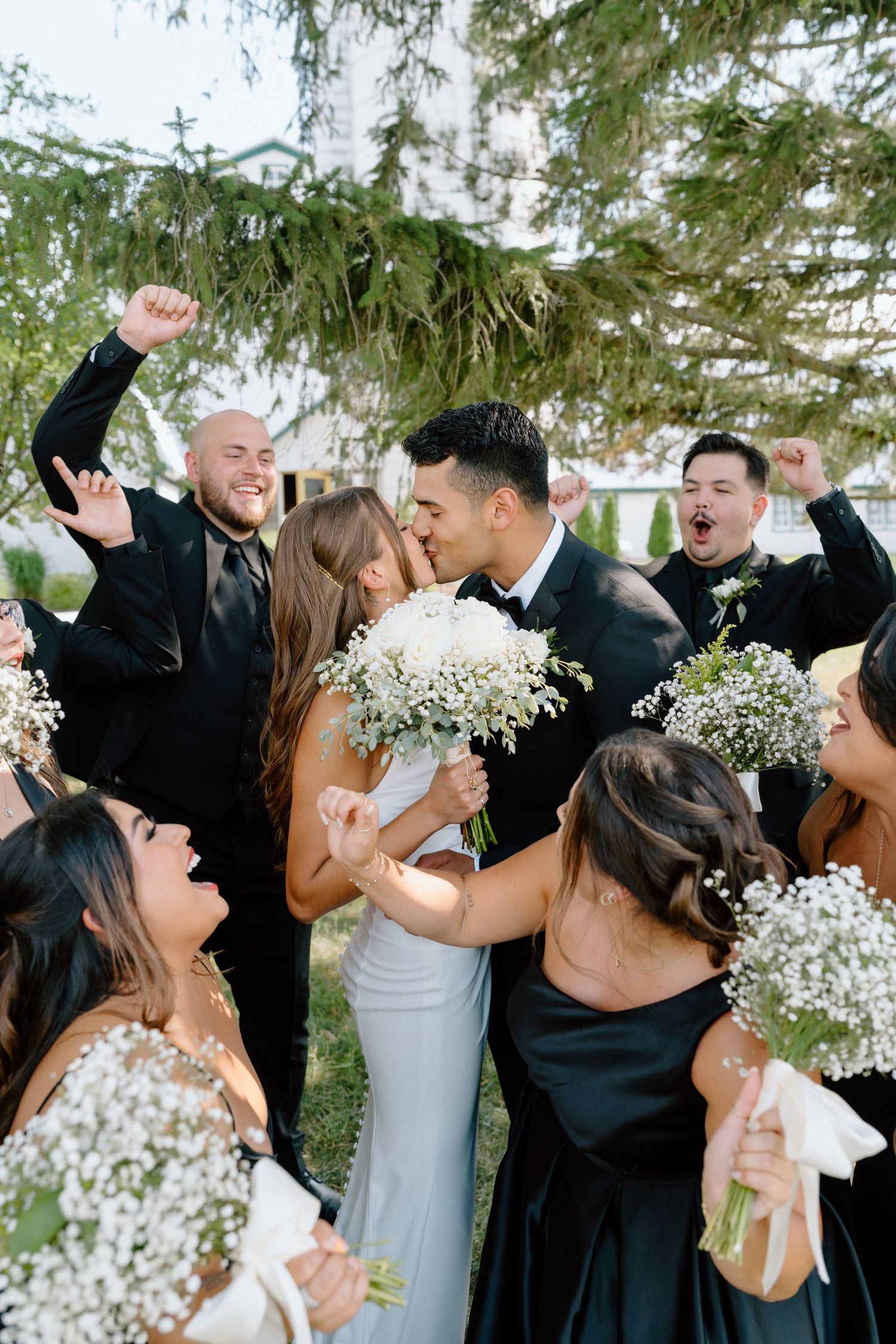 Wedding party celebrates with joyful cheers and baby's breath bouquets during an outdoor ceremony.